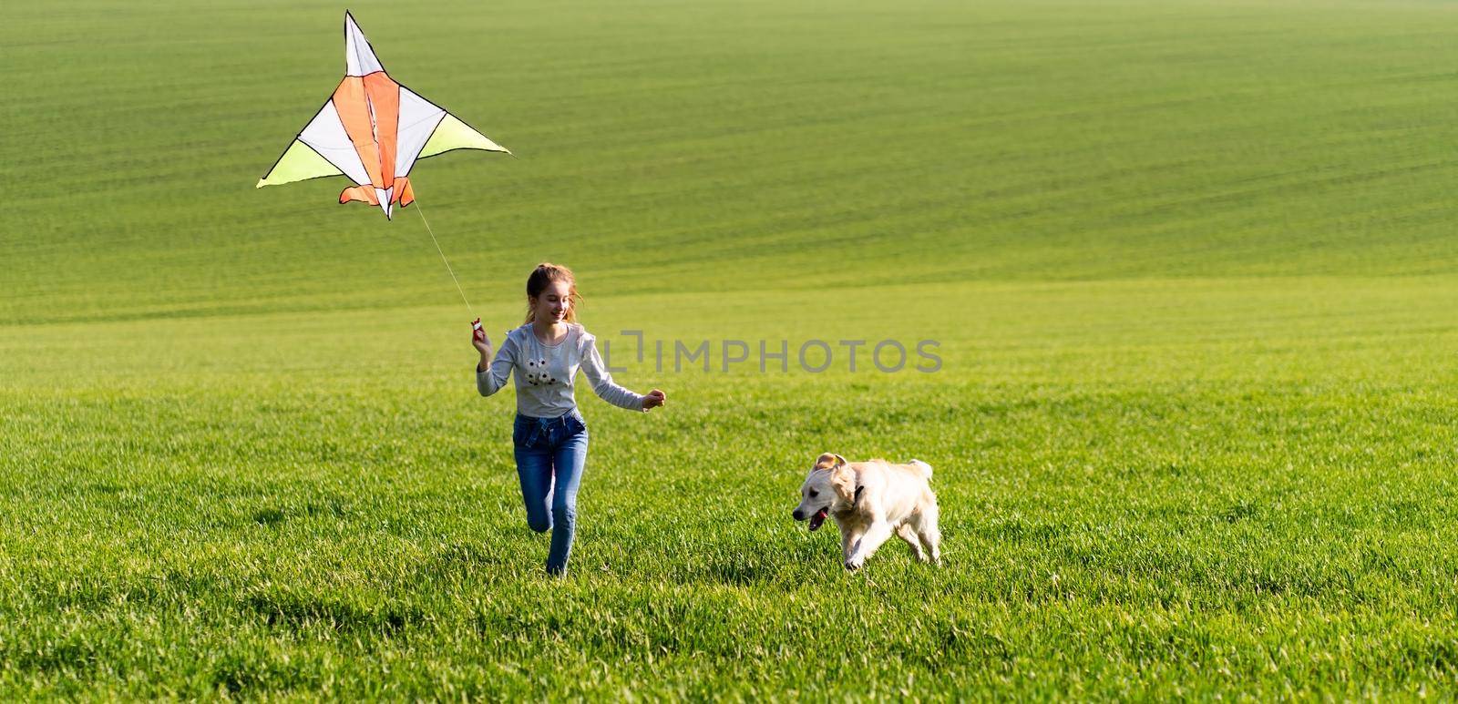 Little cute girl holding kite and running on the green grass field with dog