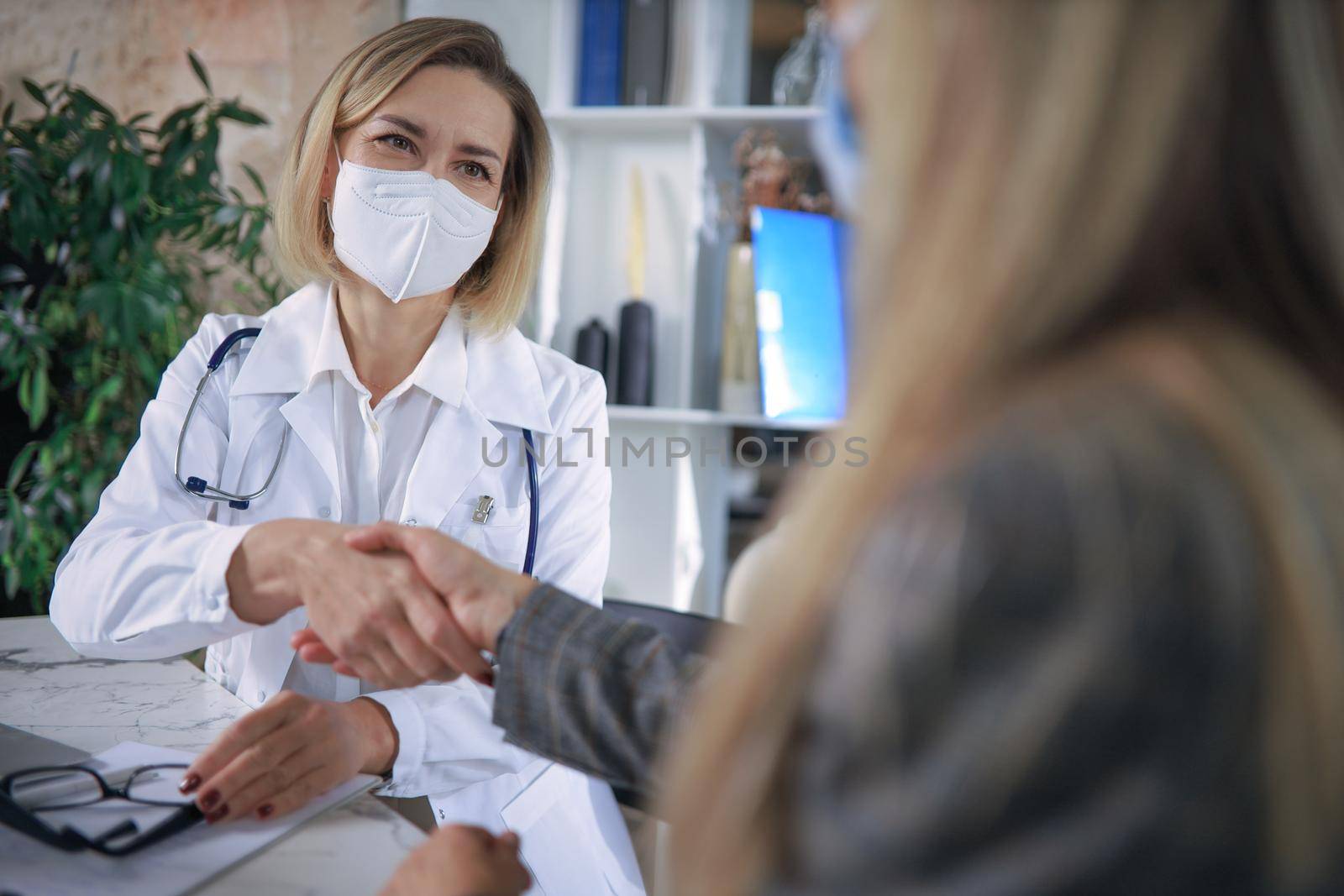 Cheerful female doctor psychologist shaking grateful patient hands after having a consultation meeting