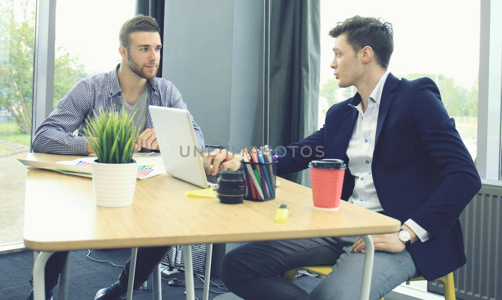 Two young modern men discussing work in the office