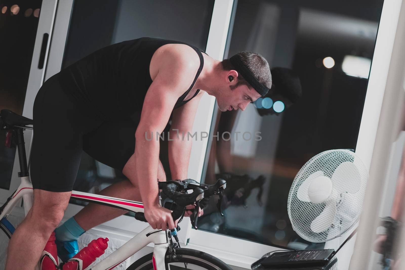 Man cycling on the machine trainer he is exercising in the home at night. Playing online bike racing game during coronavirus covid19 lockdown. New normal concept.