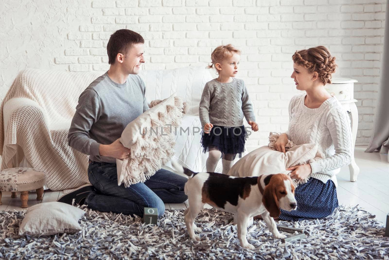 happy parents and five year old daughter playing with a pet dog in the spacious living room on Sunday