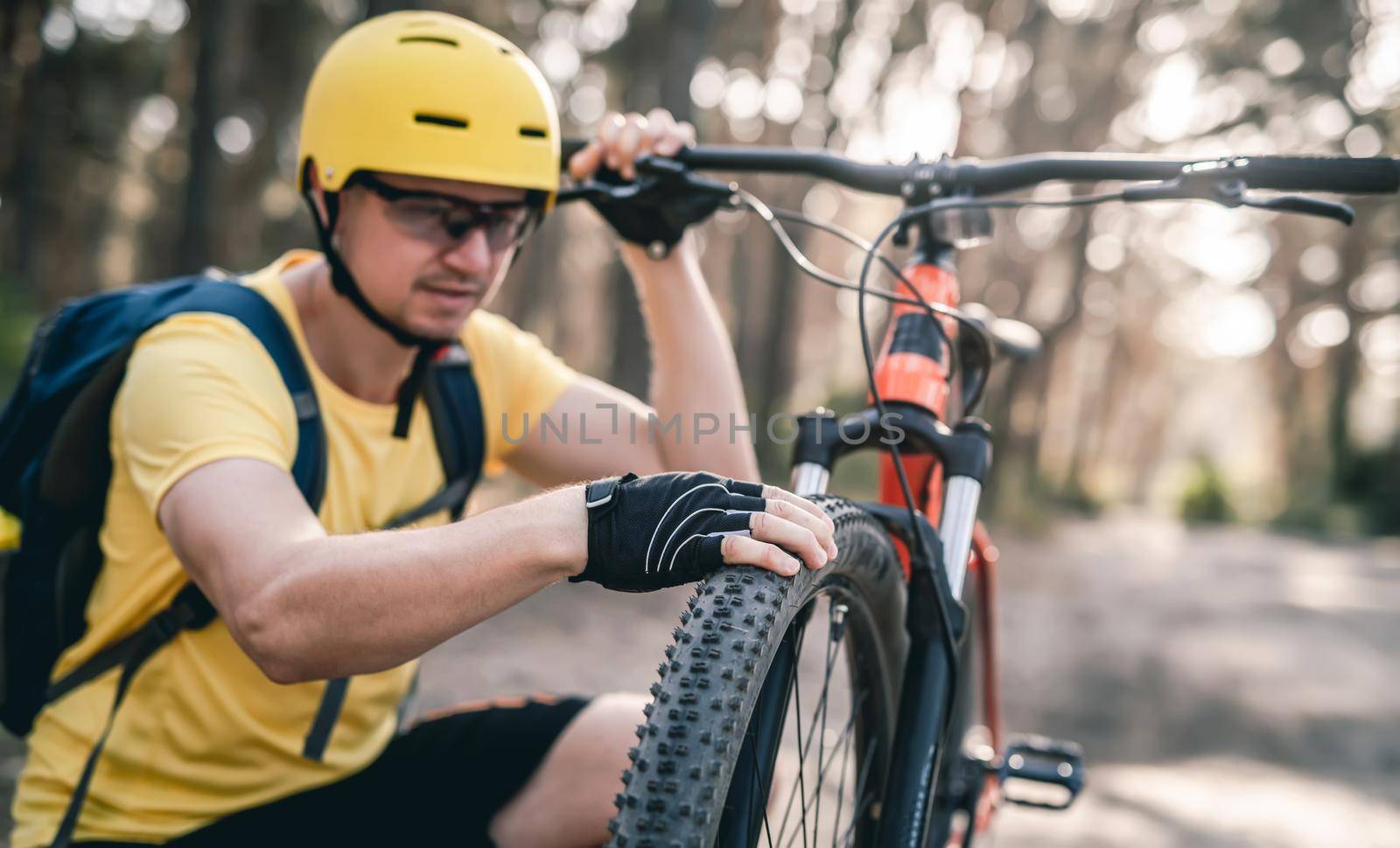 Bycyclist checking bicycle tire pressure before ride in forest