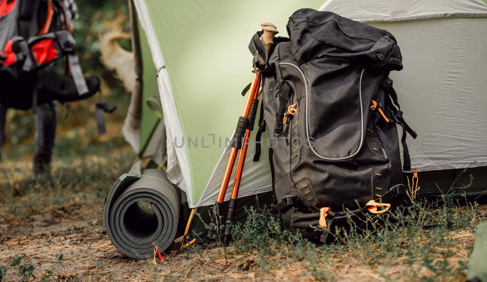 Black backppack and karemat close to tent in camping place in the forest. View on travel touristic hiking equipment outdoor
