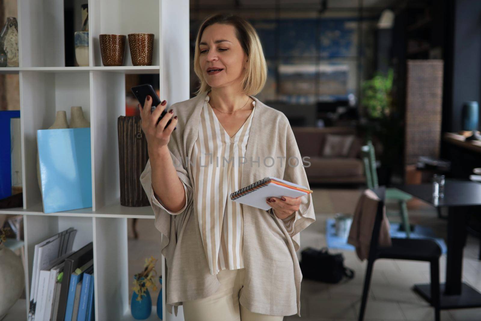 Beautiful business woman is using her smartphone with smile while standing in the office