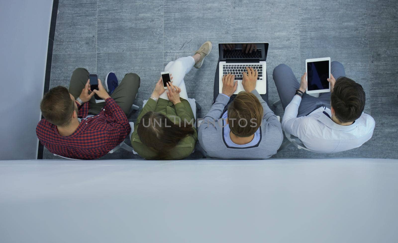 Group of attractive young people sitting on the floor using a laptop, Tablet PC, smart phones, smiling.