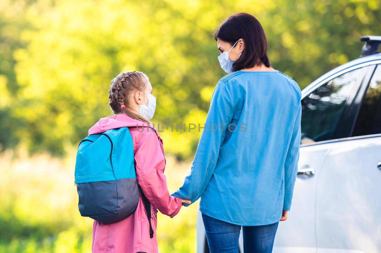 Mother meeting daughter after school during pandemic next to car at sunny day