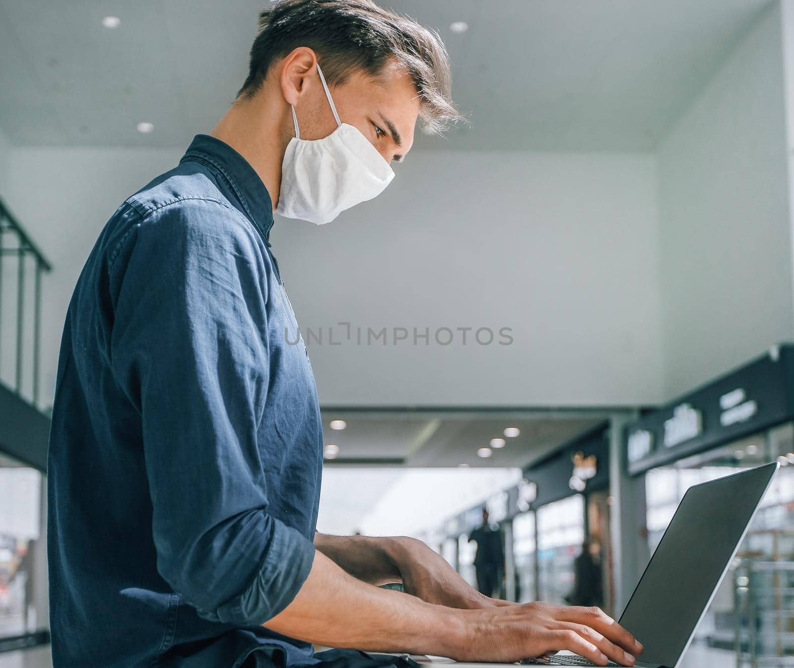 man in a protective mask works on a laptop in a shopping center building. pandemic in the city