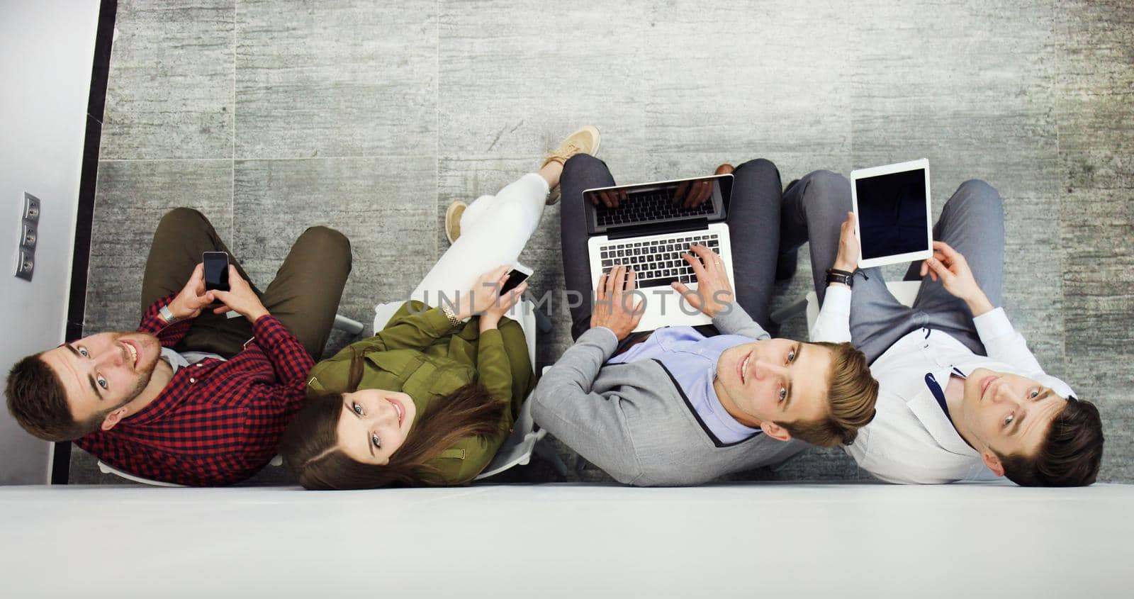 Group of attractive young people sitting on the floor using a laptop, Tablet PC, smart phones, smiling.