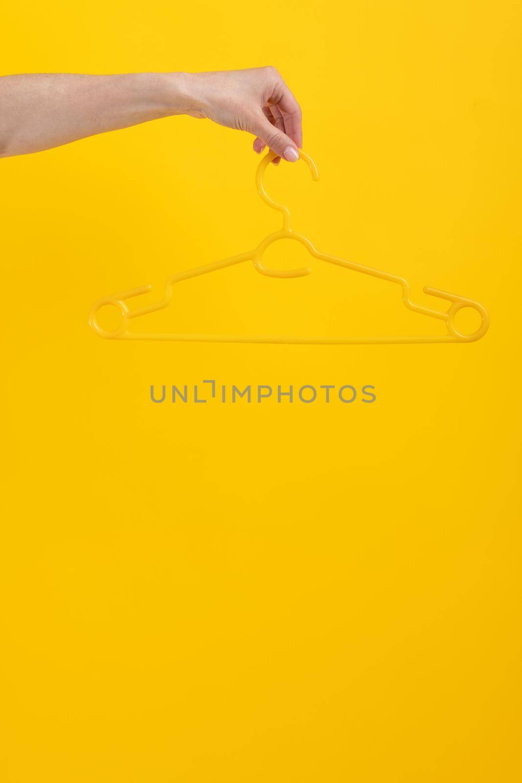 Hand holding hanger isolated on yellow background with copyspace. Stylish design look on fashion accessory. Concept of clothes retail