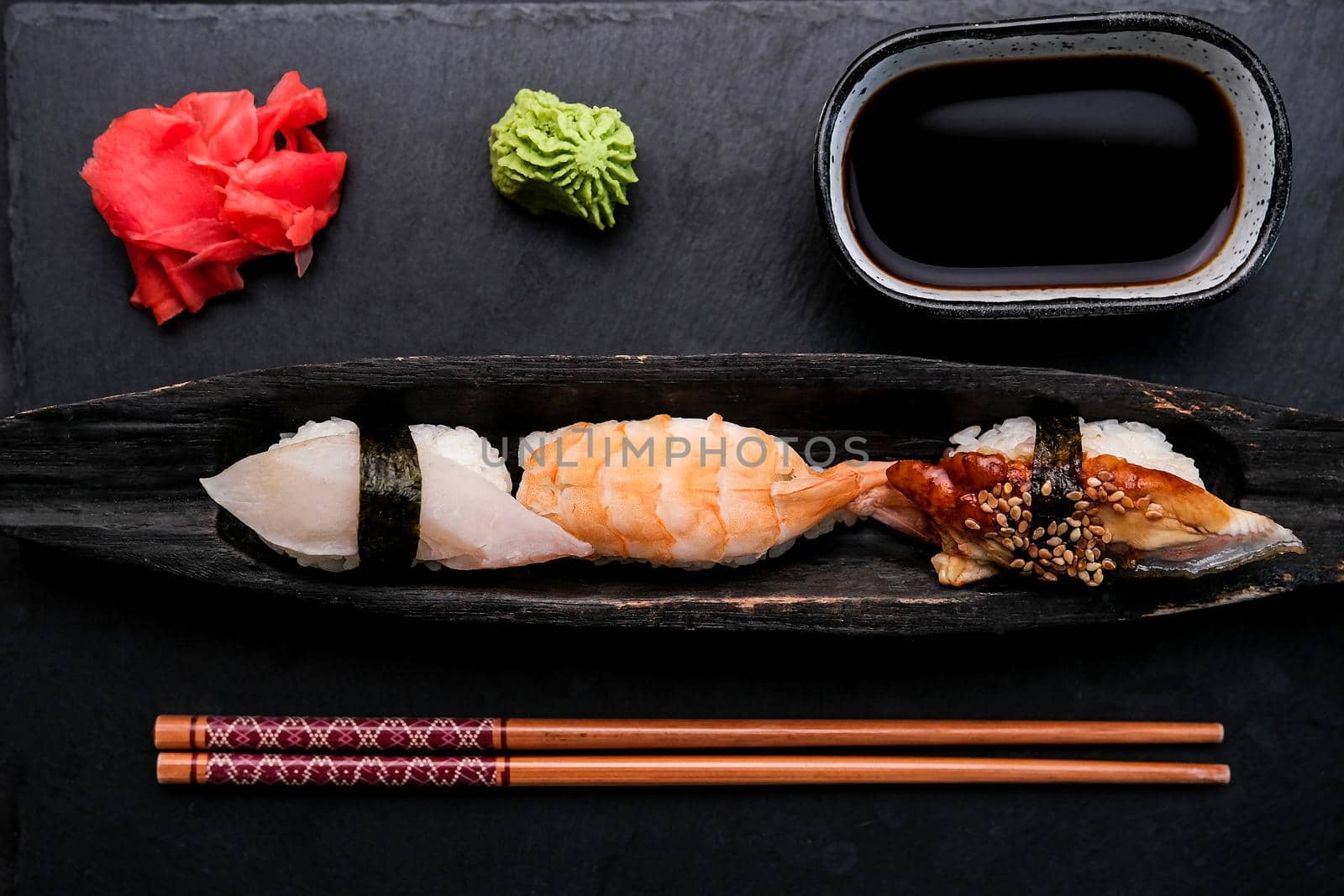 Elegant served sushi set composition with fresh shrimp and raw salmon on black plate with ginger, wasabi and soy sauce shooting from above. Traditional japanese meal with wooden chopstick