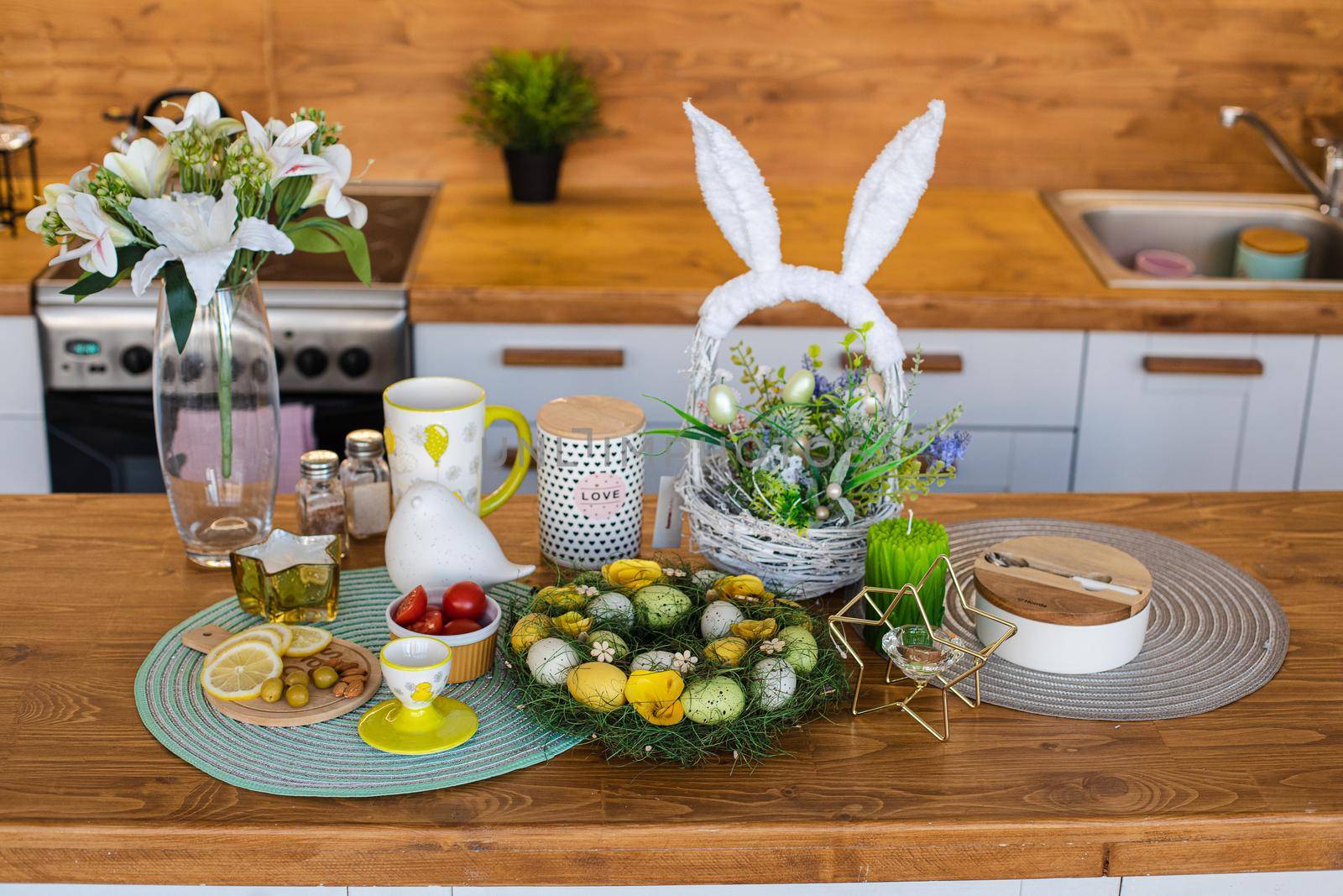 Easter celebration on wooden kitchen counter. Dyed eggs with snacks and basket with bunny ears on wooden counter.