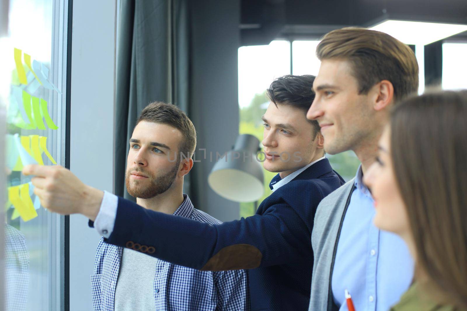 young creative startup business people on meeting at modern office making plans and projects with post stickers on glass