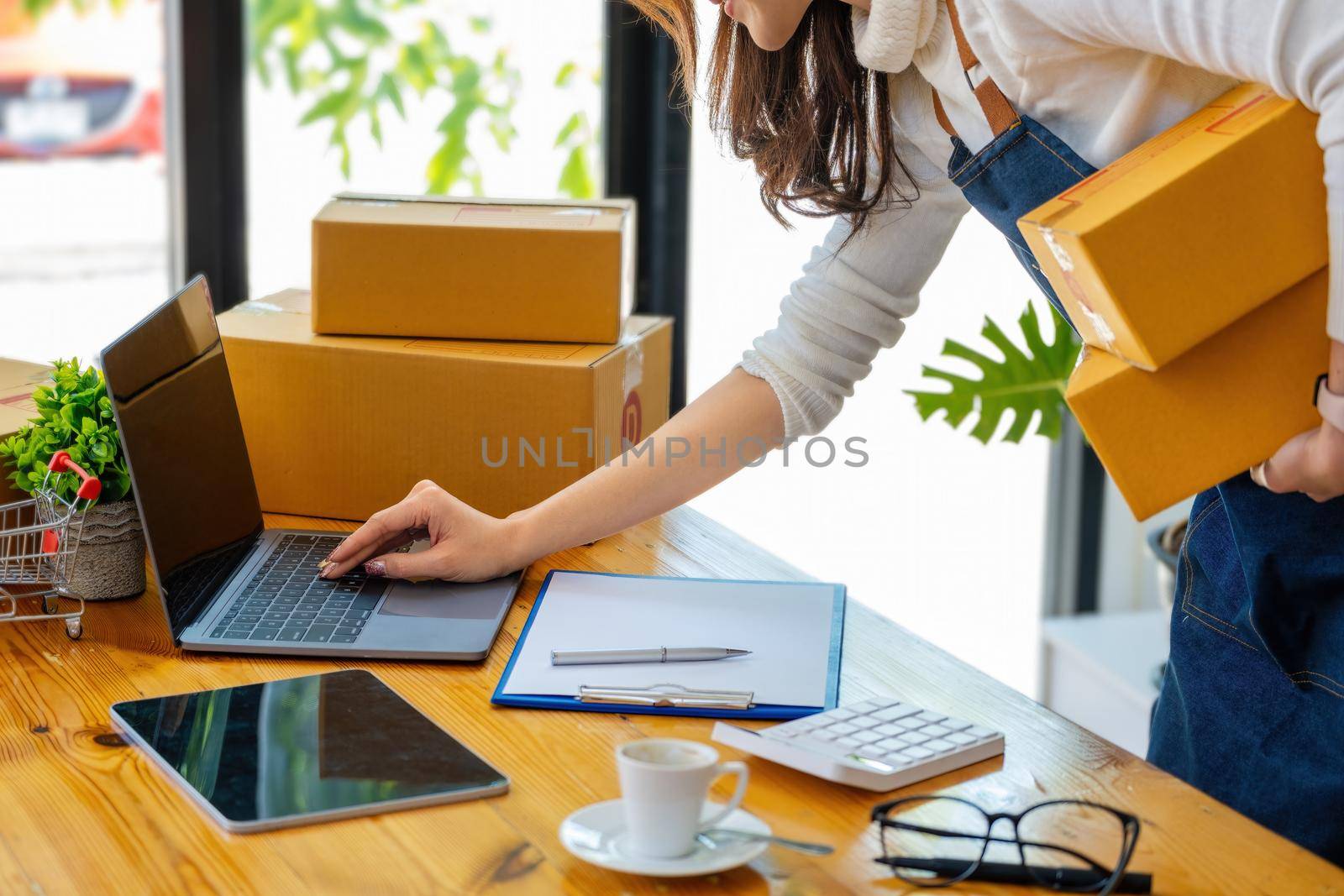 Work from home. happy women selling products online Start a small business owner by using laptop computer to calculate prices and prepare for postage. by Manastrong