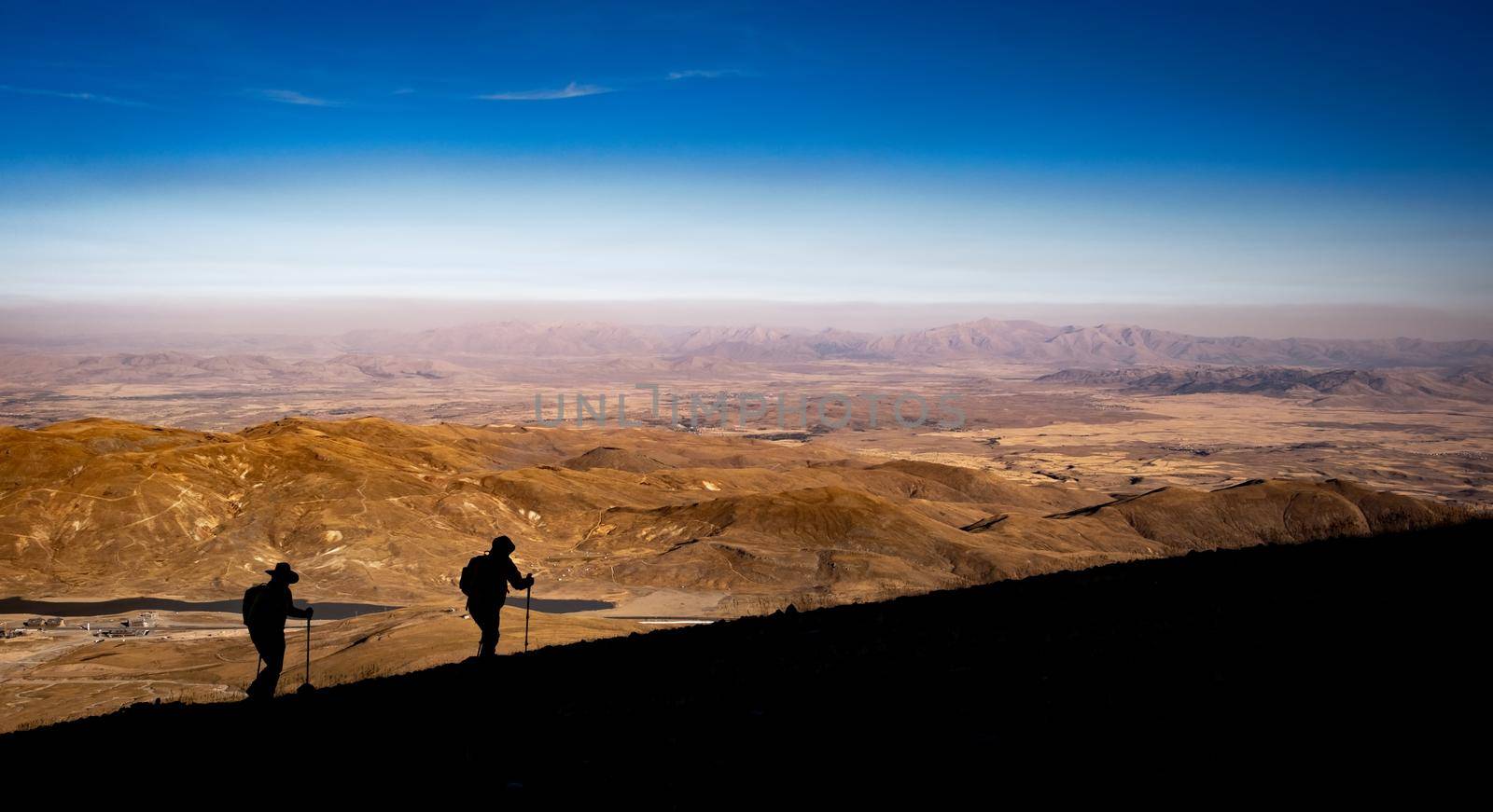 Silhouettes of two people during hiking on volcano Erciyes in Turkey in sunrise time. People climbing to mountain and looking from the top on beautiful hills. Scenery Kayseri landscapes with blue sky