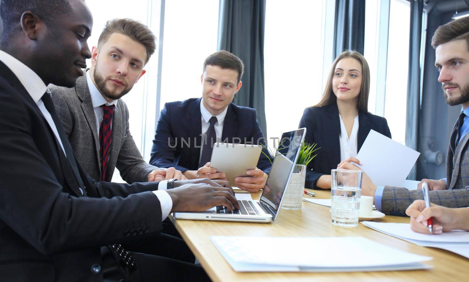 Young handsome woman gesturing and discussing something while his coworkers listening to him sitting at the office table