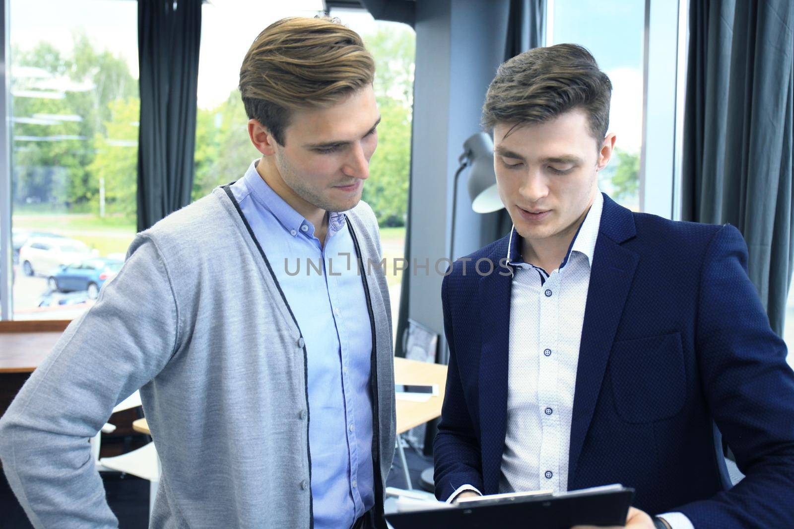 Two young modern men discussing work in the office