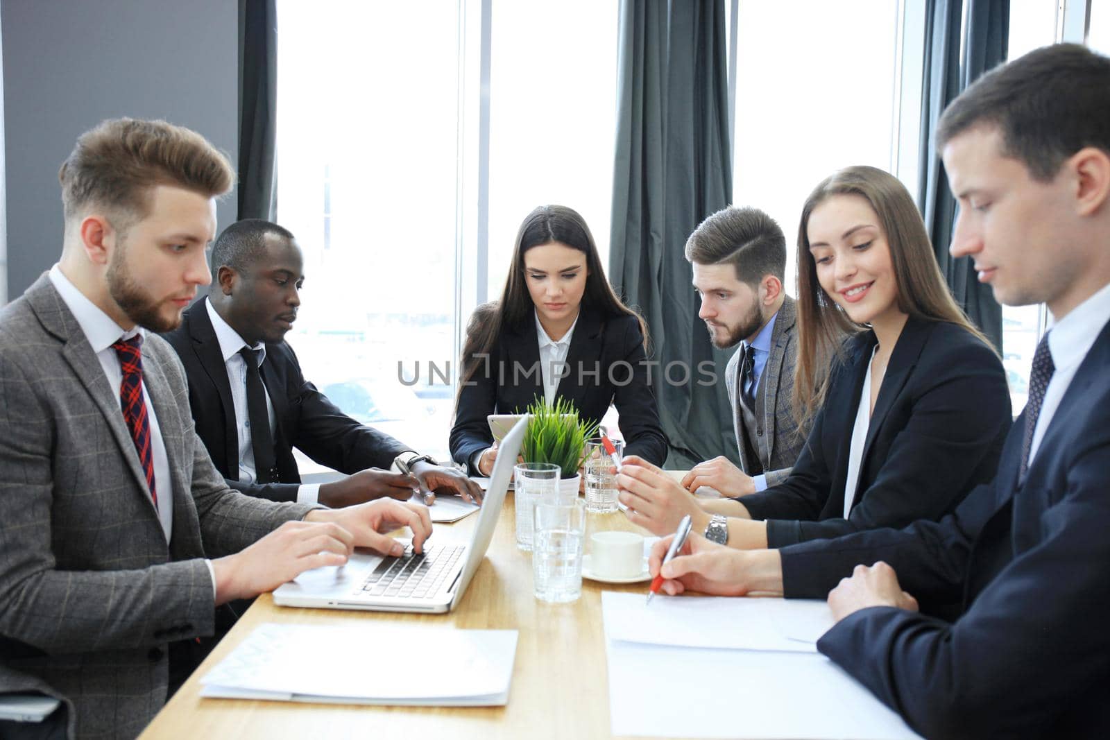 Young handsome woman gesturing and discussing something while his coworkers listening to him sitting at the office table