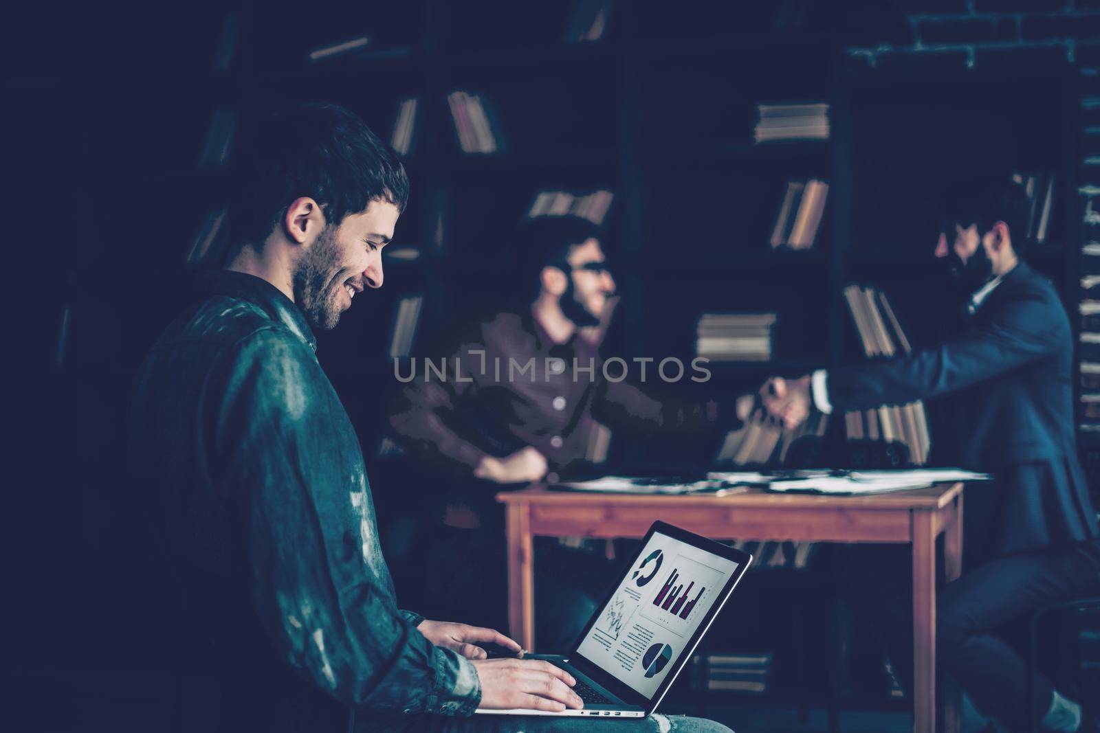 sales Manager working on laptop with a marketing report on the background of business partners handshaking