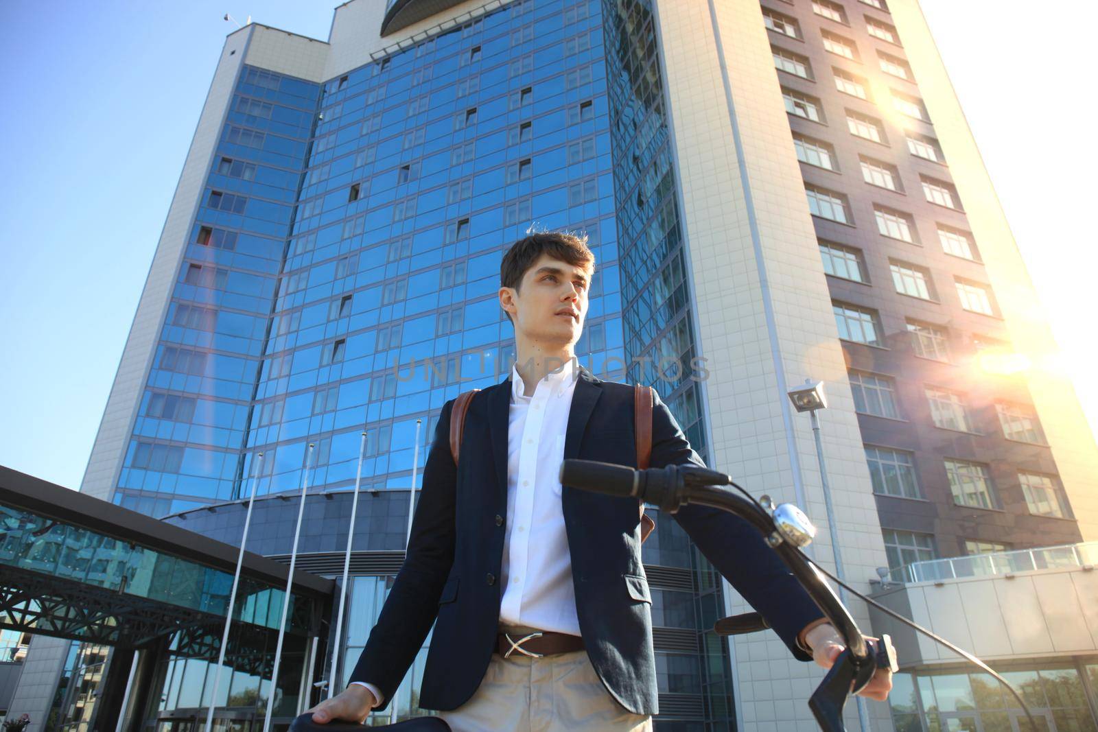 Confident young businessman walking with bicycle on the street in town.