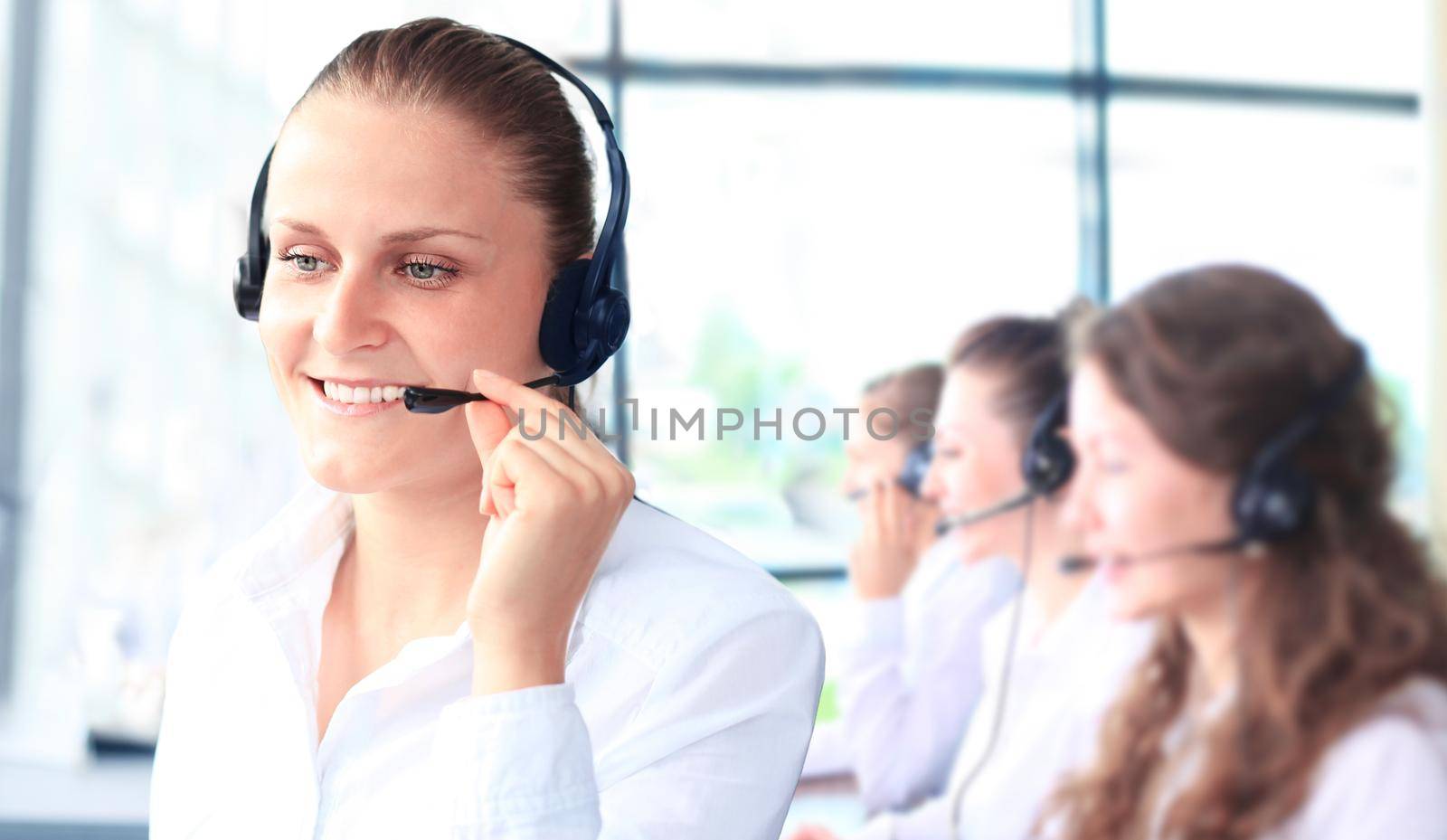 Smiling female customer service representative talking on headset with colleagues in background at office