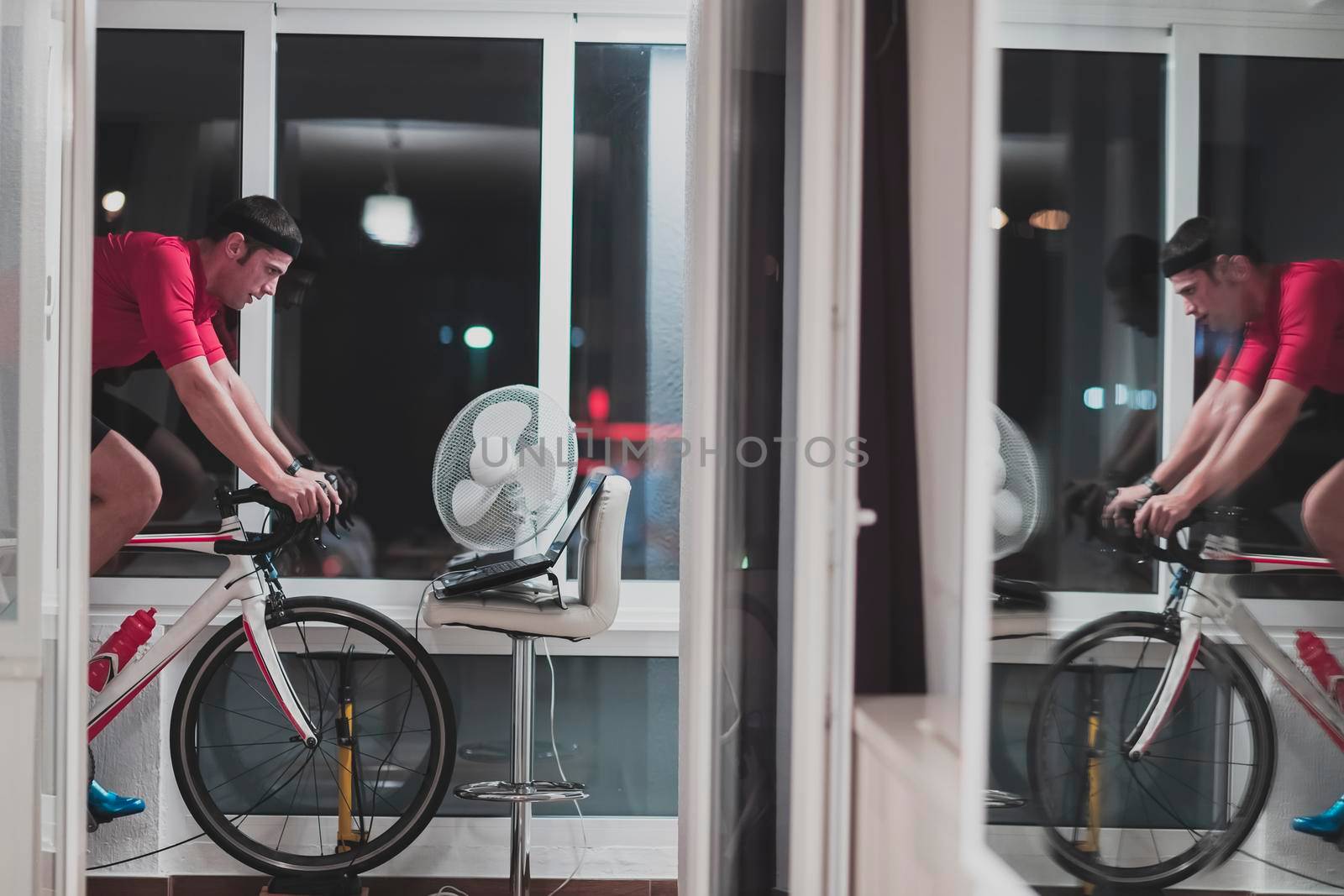 Man cycling on the machine trainer he is exercising in the home at night playing online bike racing game by dotshock