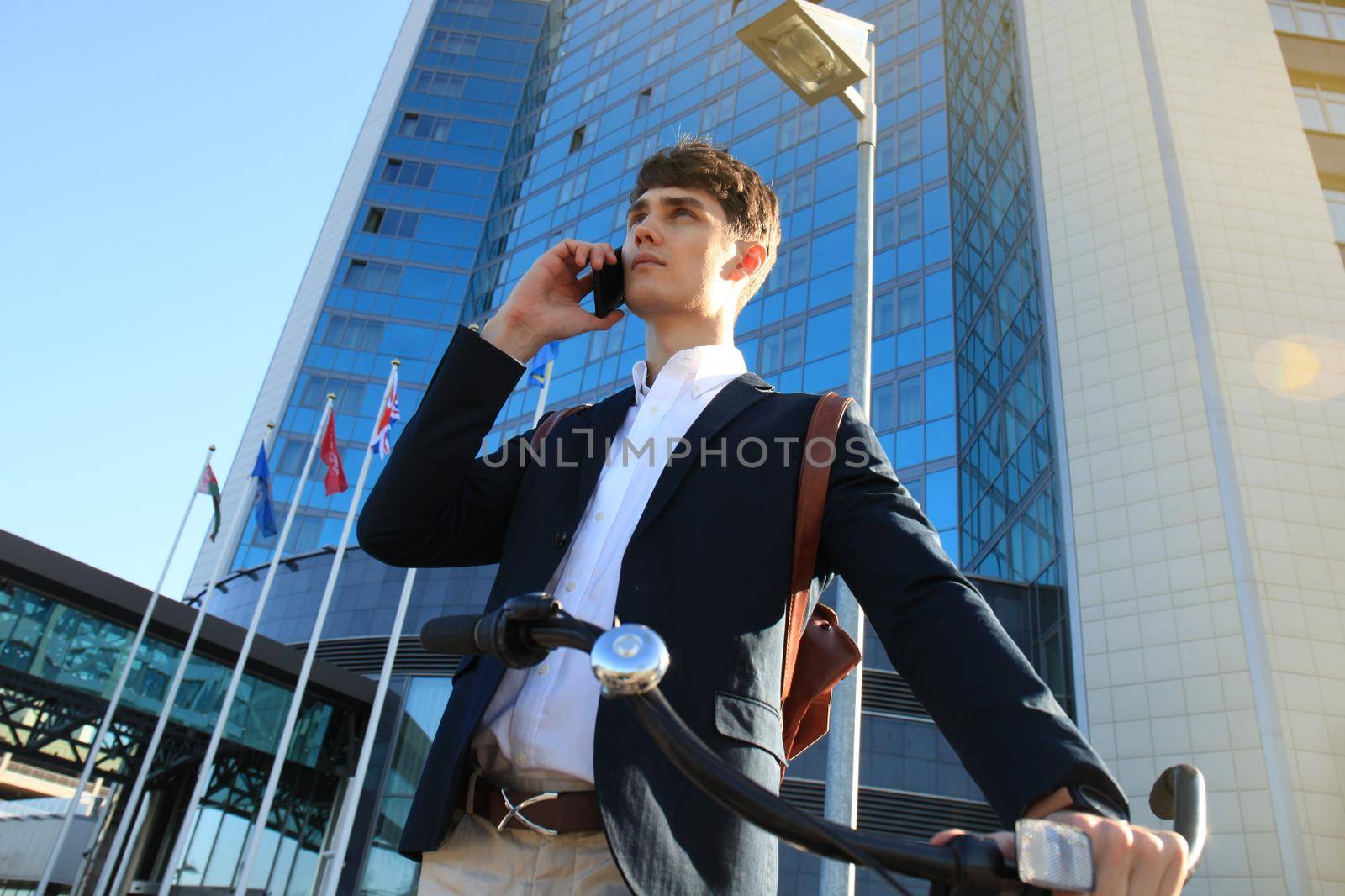 Young businessman with bicycle and smartphone on city street.
