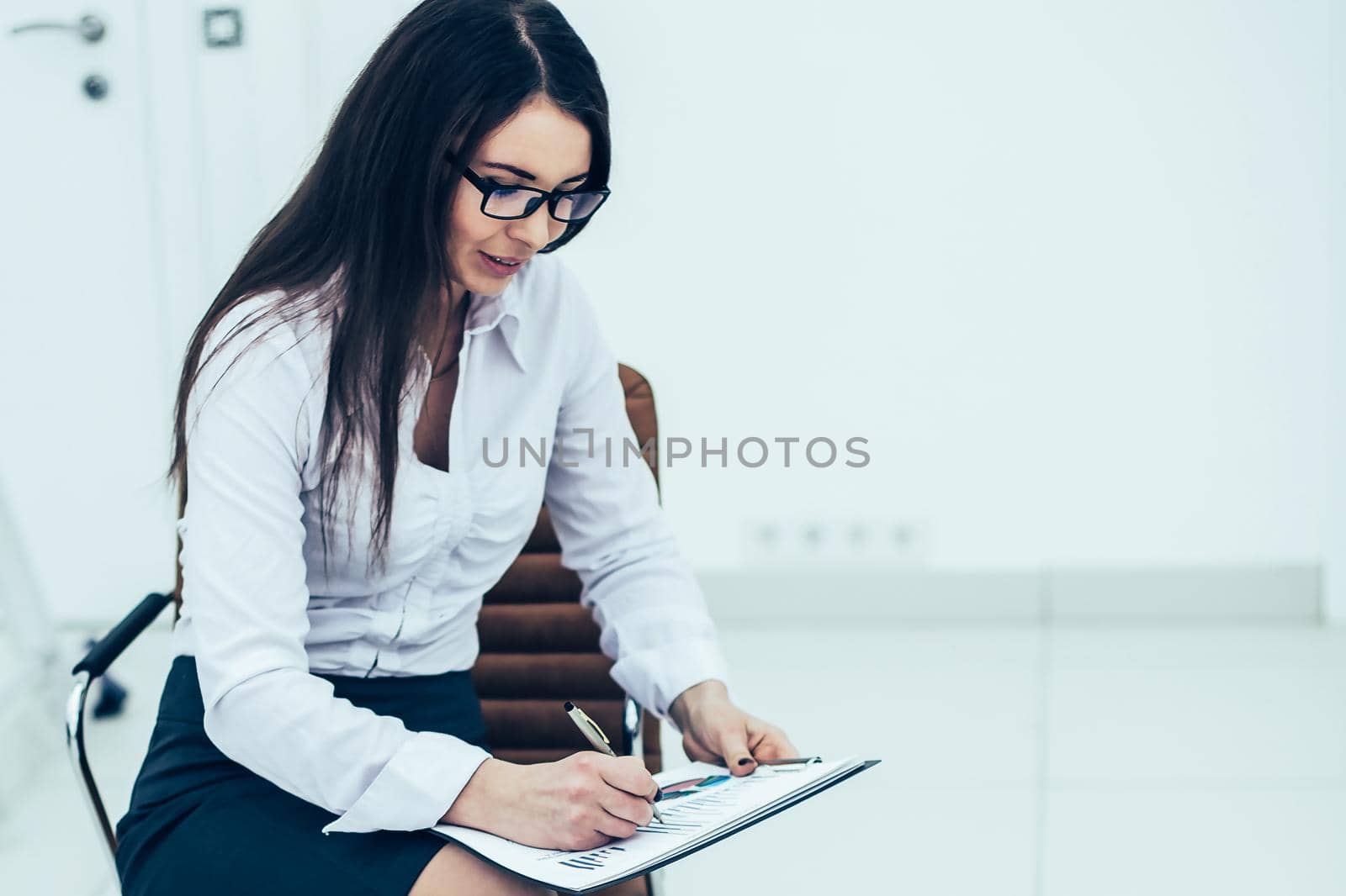 business woman with documents and financial charts sitting on a chair in the spacious office.the photo has a empty space for your text