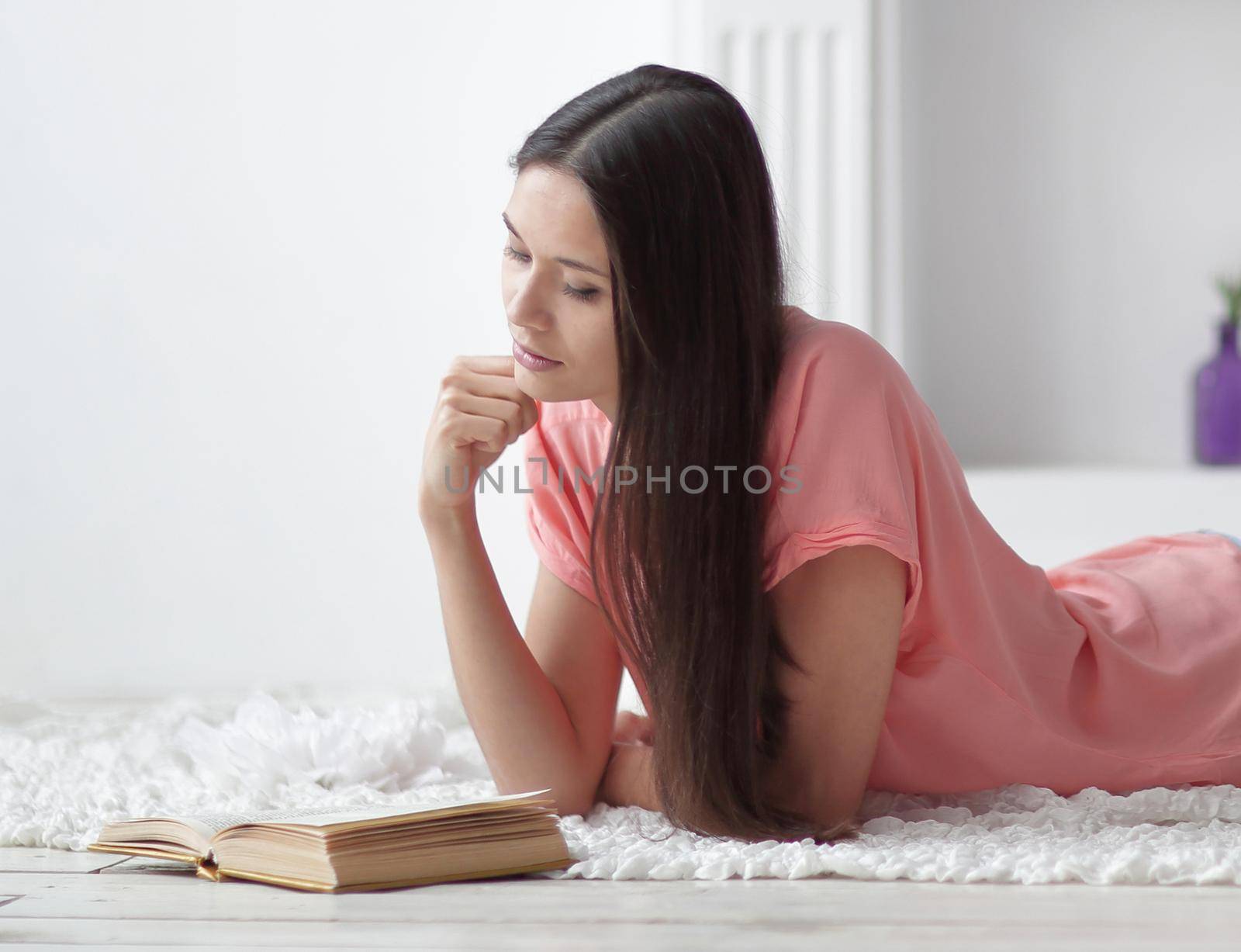 portrait of young girl reading book lying on floor in living room.