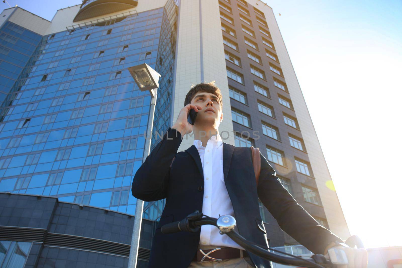 Young businessman with bicycle and smartphone on city street.