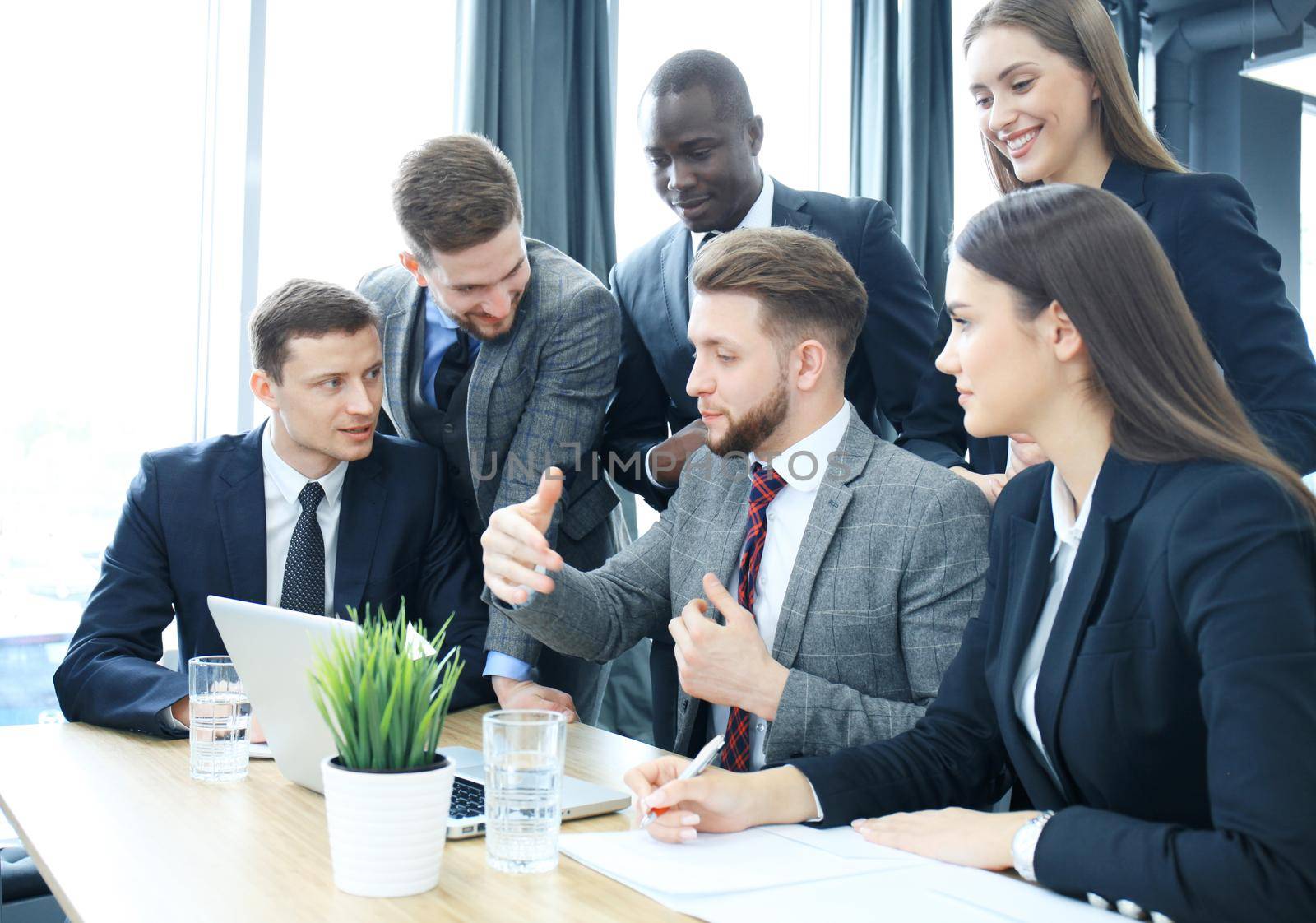 Brainstorm. Group of business people looking at the laptop together. One business woman looking at camera