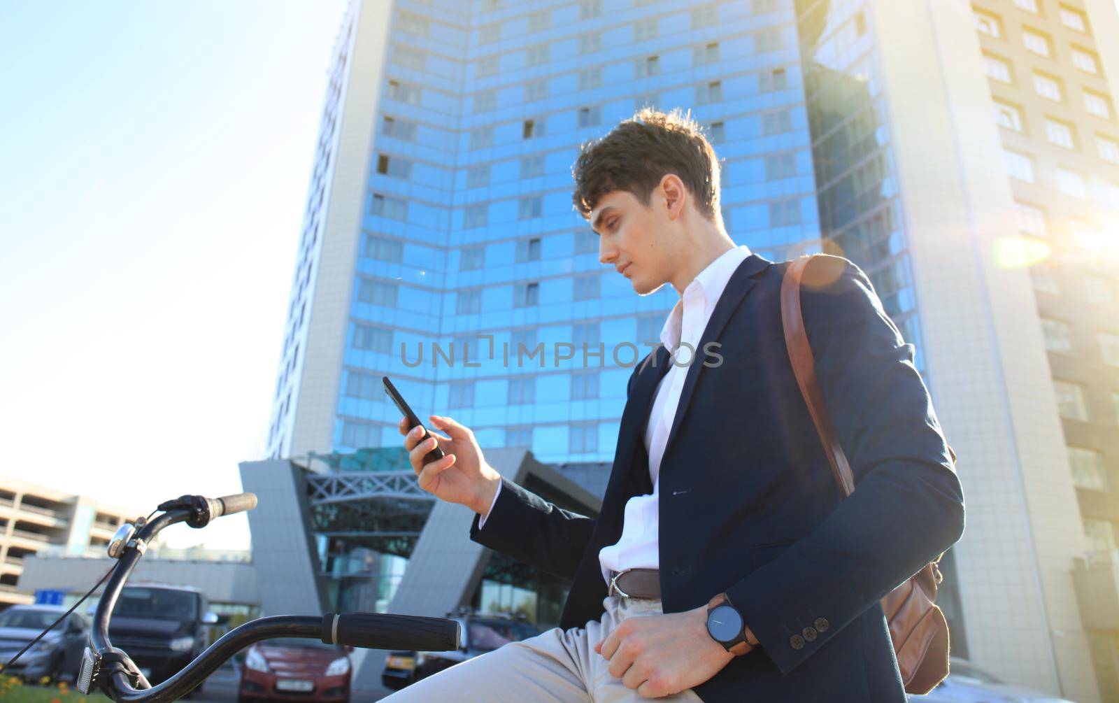 Young businessman with bicycle and smartphone on city street.