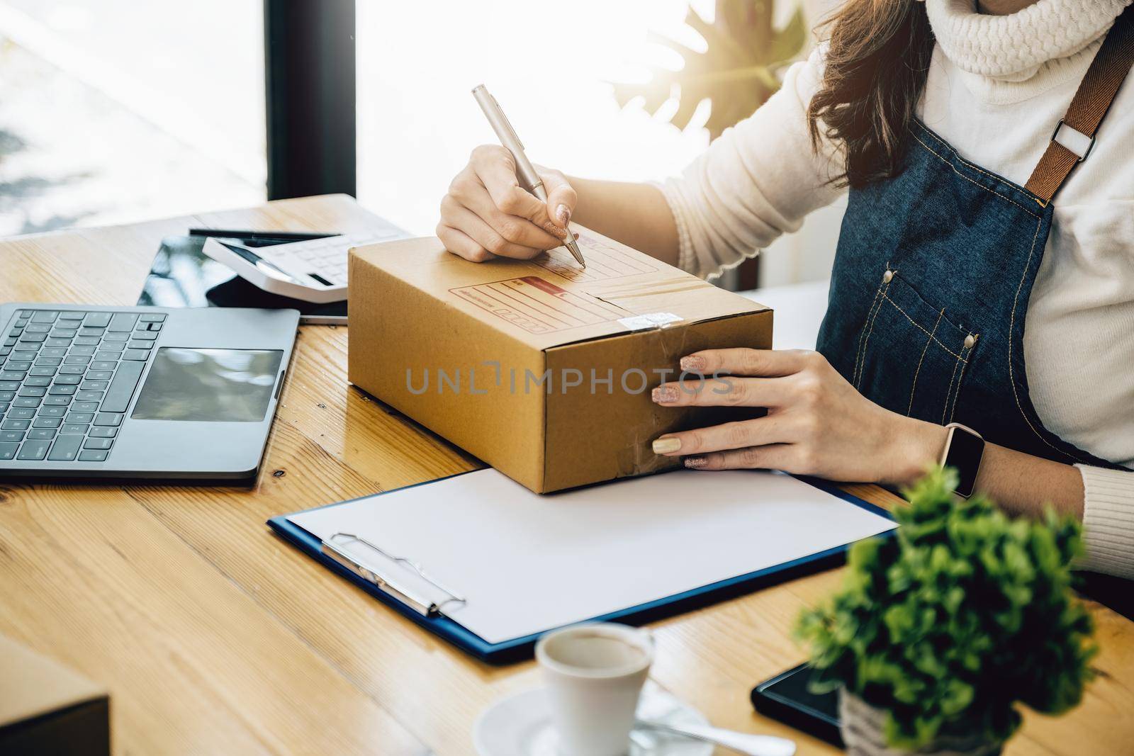 Business owners use pens to write on parcel boxes and use computers to check online orders to prepare packaged boxes. Pack products for delivery to customers. by Manastrong