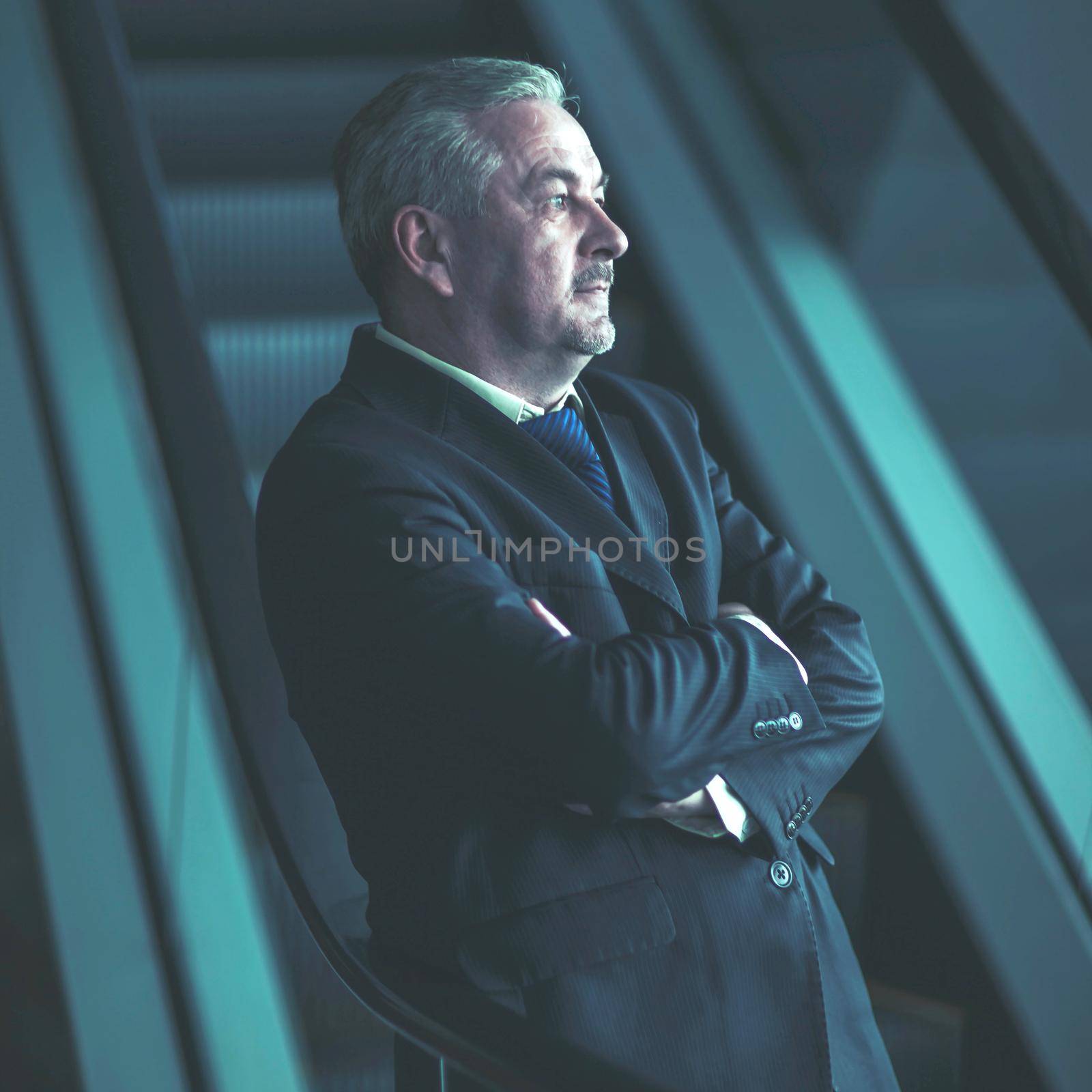 successful businessman standing on the stairs of a modern office on a dark background by SmartPhotoLab