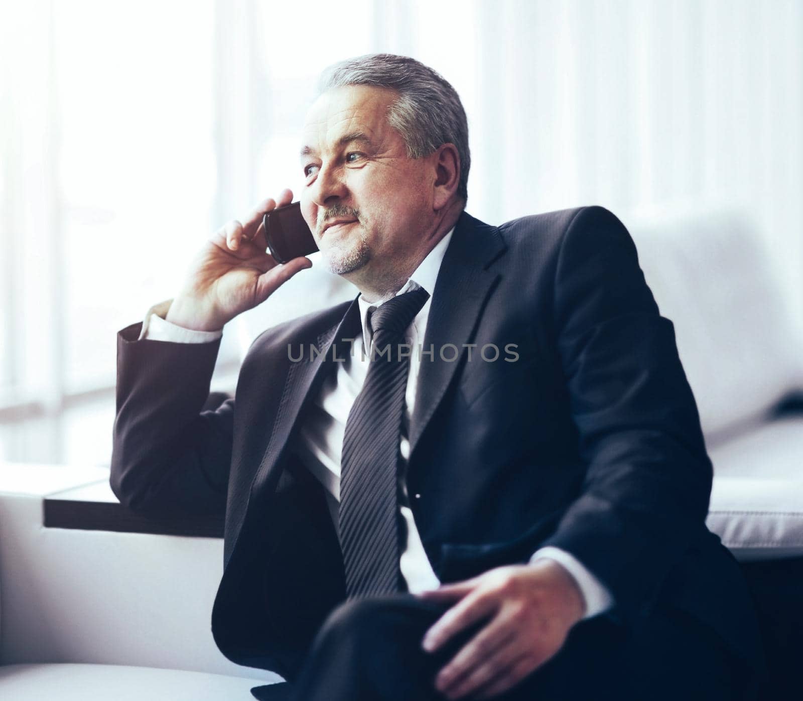 Businessman in the office sitting on the couch talking on the phone and looking out the window