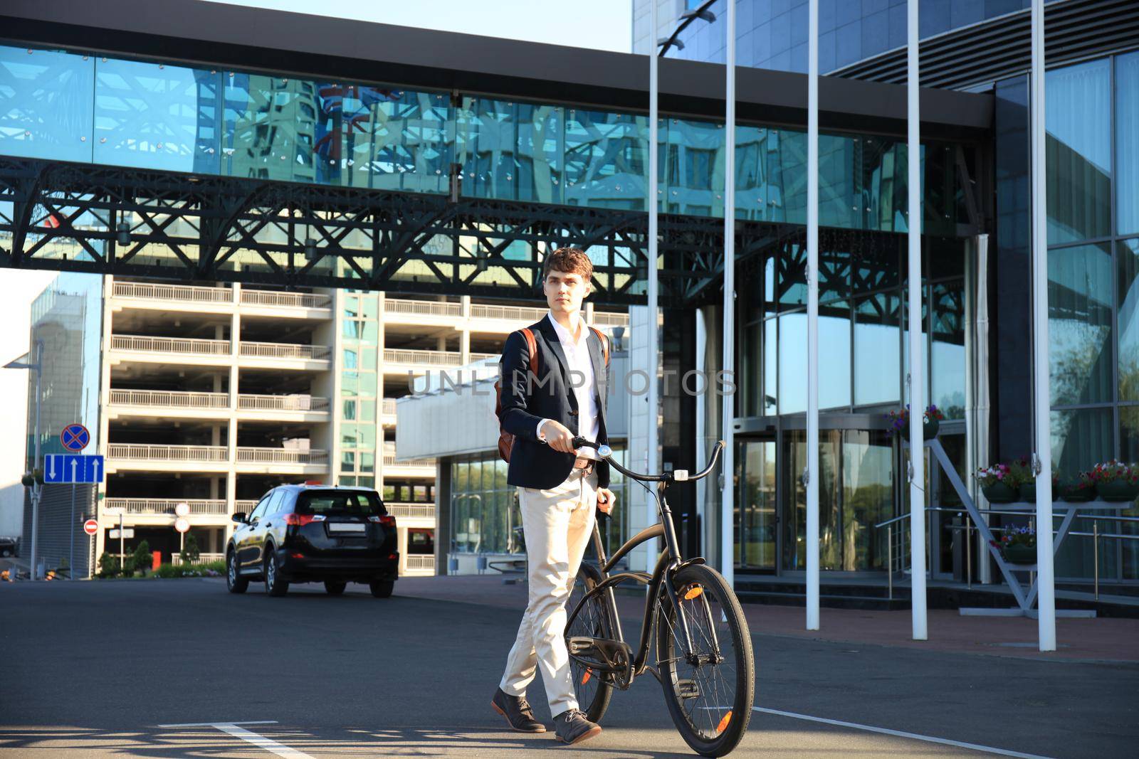 Confident young businessman walking with bicycle on the street in town.