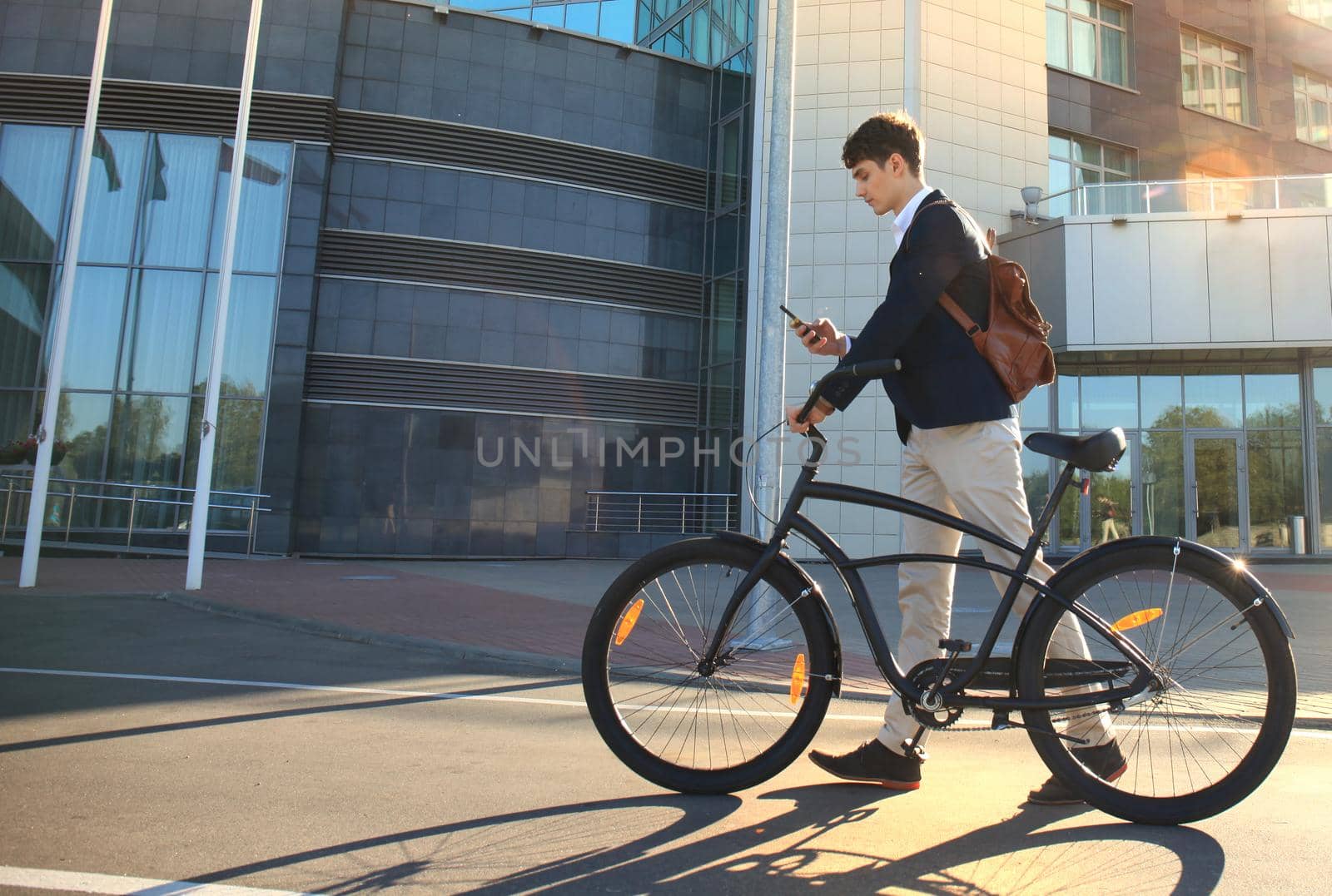 Young businessman with bicycle and smartphone on city street.