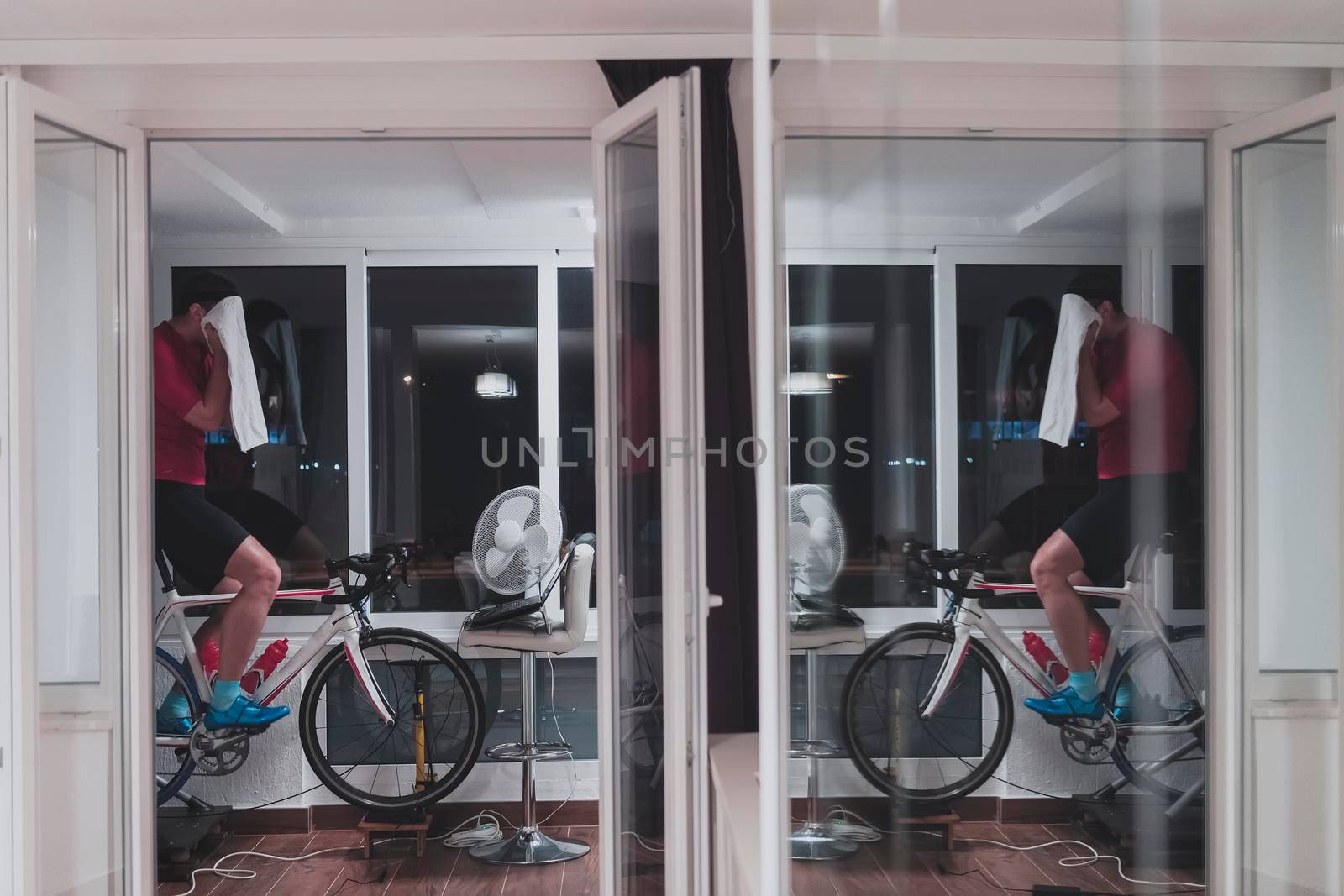 Man cycling on the machine trainer he is exercising in the home at night playing online bike racing game by dotshock