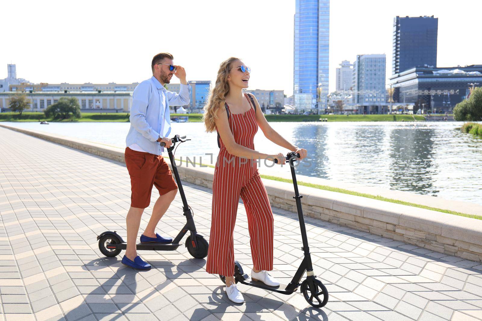 Lovely couple having fun driving electric scooter along the city promenade by tsyhun