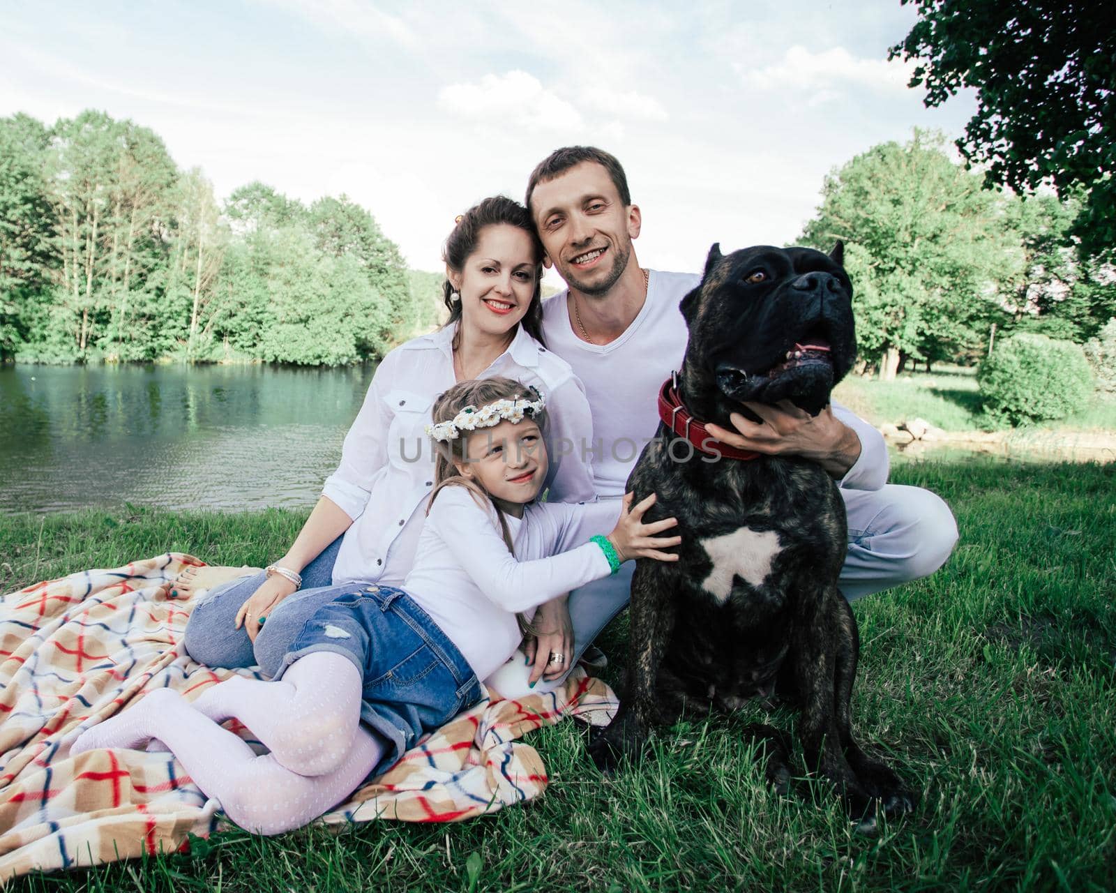 happy family with their big dog sitting on the grass near the river. the concept of family happiness