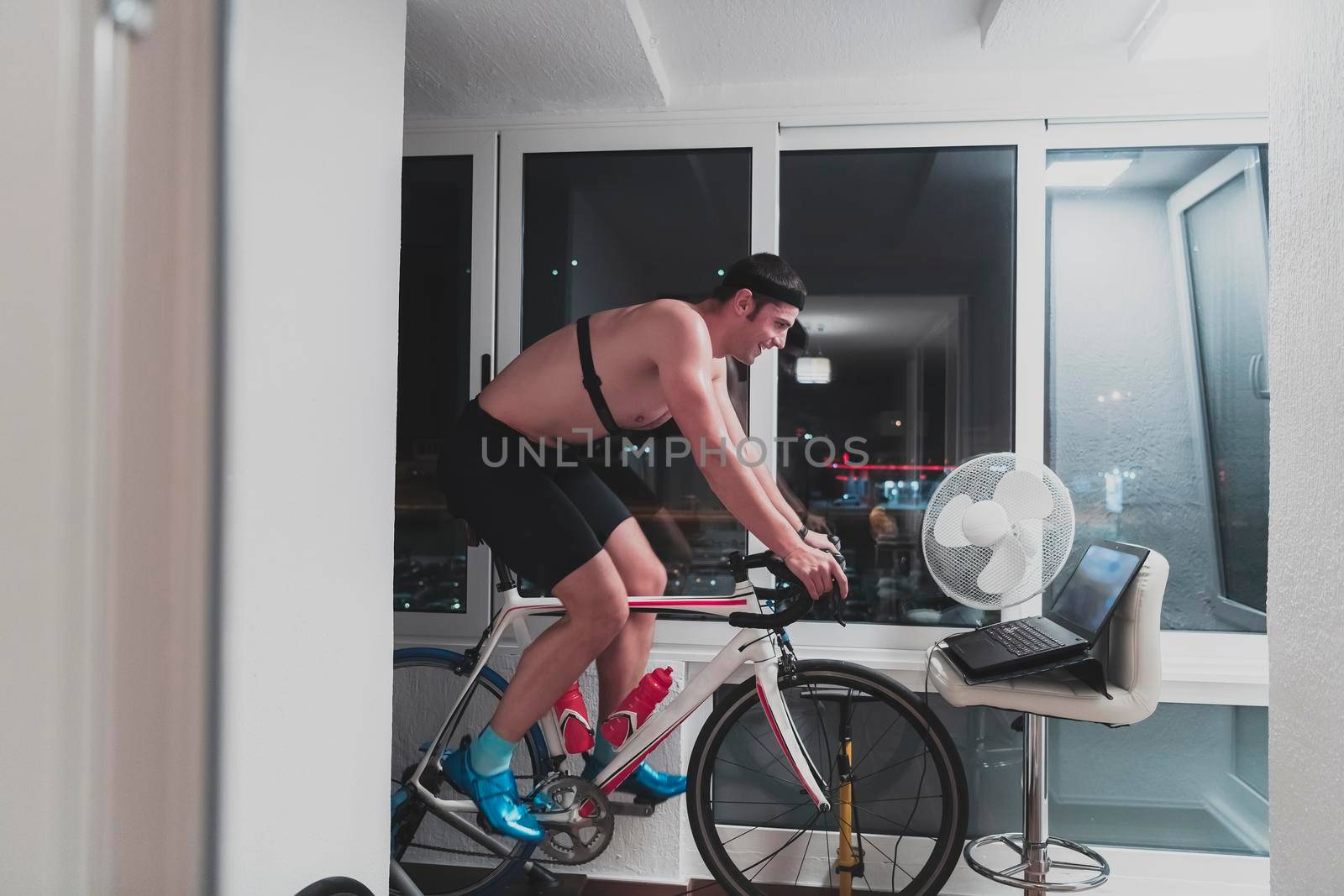 Man cycling on the machine trainer he is exercising in the home at night playing online bike racing game by dotshock