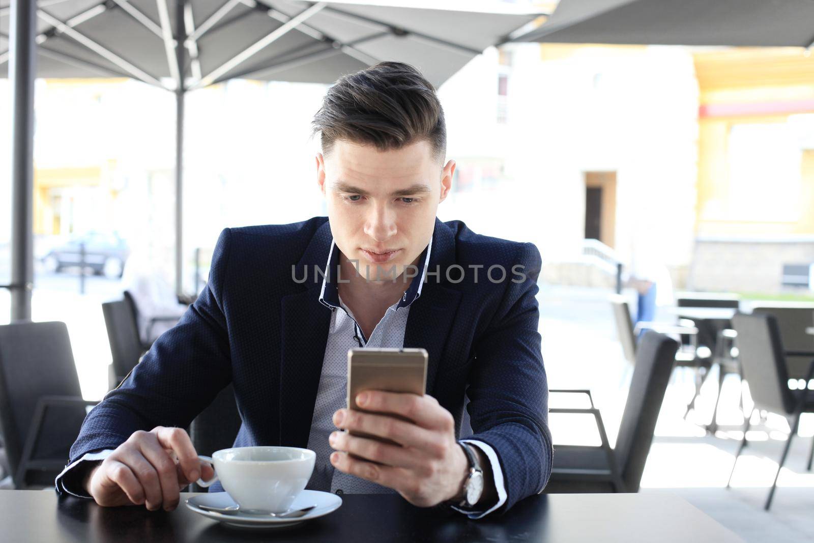 business man drinking a cup of coffee while sitting with his phone in cafe.