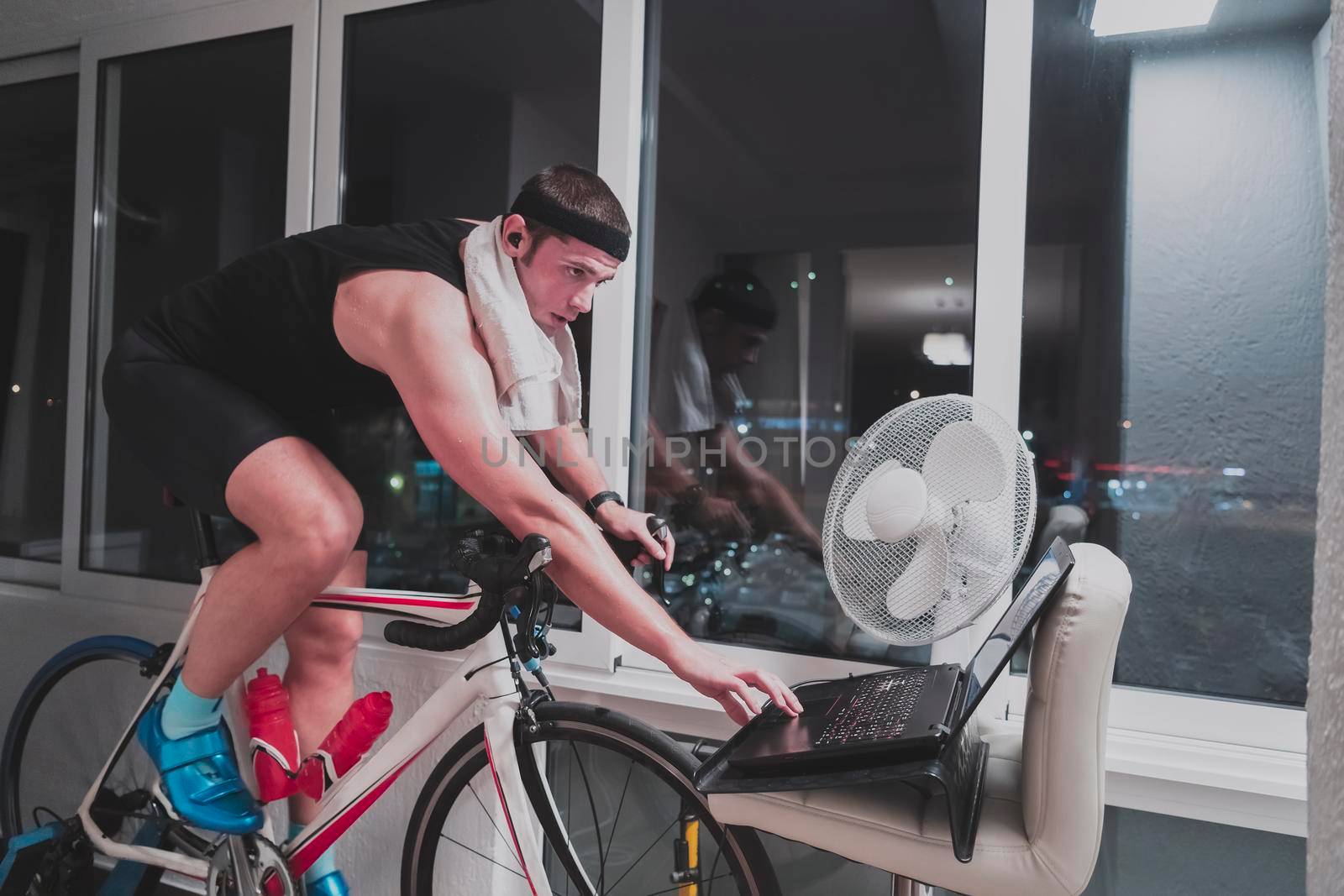 Man cycling on the machine trainer he is exercising in the home at night. Playing online bike racing game during coronavirus covid19 lockdown. New normal concept.