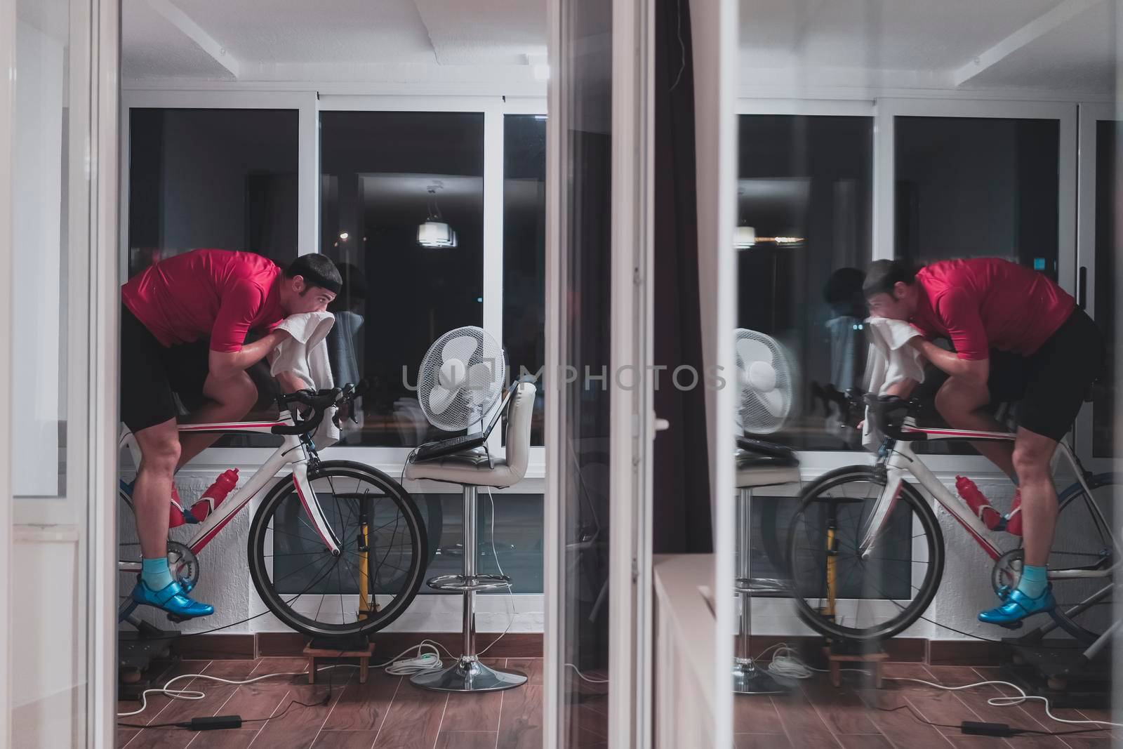 Man cycling on the machine trainer he is exercising in the home at night. Playing online bike racing game during coronavirus covid19 lockdown. New normal concept.