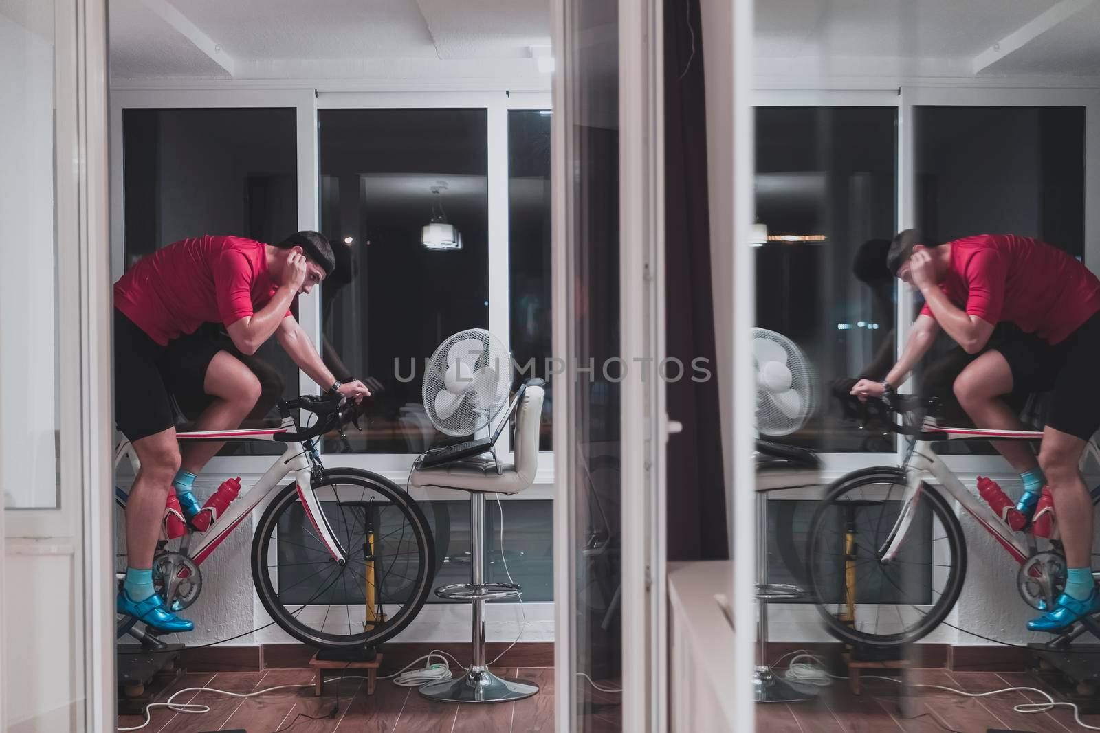 Man cycling on the machine trainer he is exercising in the home at night. Playing online bike racing game during coronavirus covid19 lockdown. New normal concept.