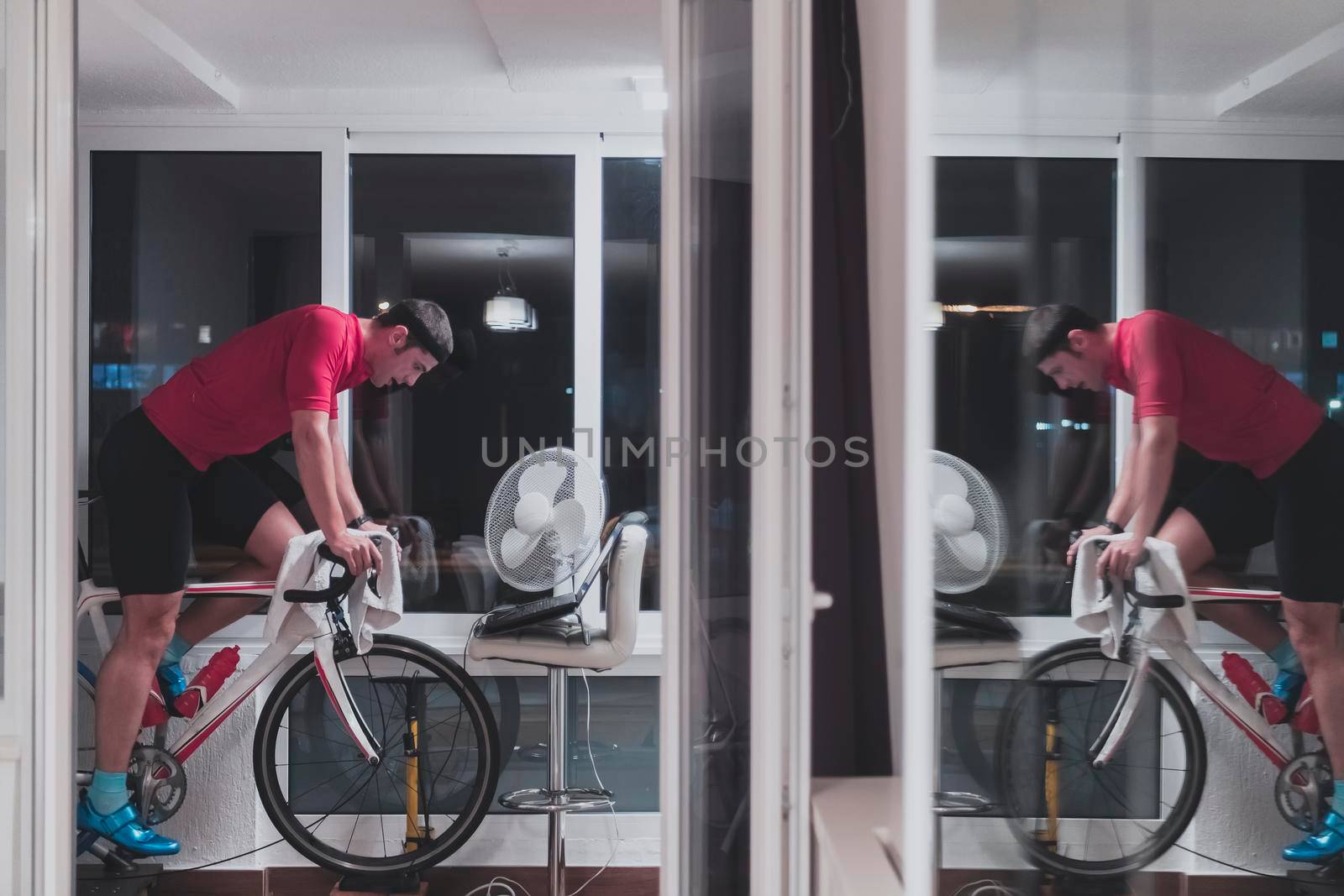 Man cycling on the machine trainer he is exercising in the home at night. Playing online bike racing game during coronavirus covid19 lockdown. New normal concept.