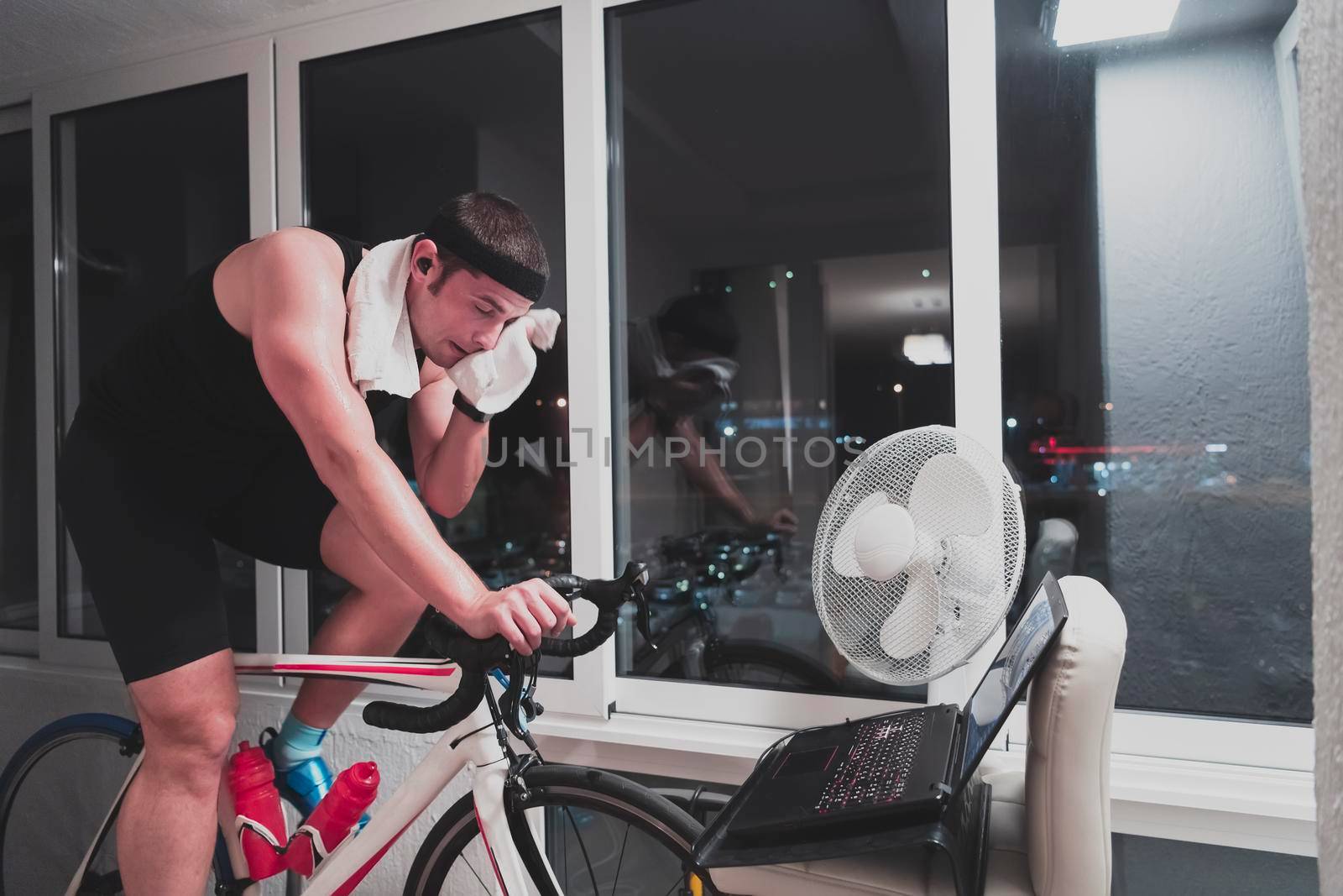 Man cycling on the machine trainer he is exercising in the home at night playing online bike racing game by dotshock