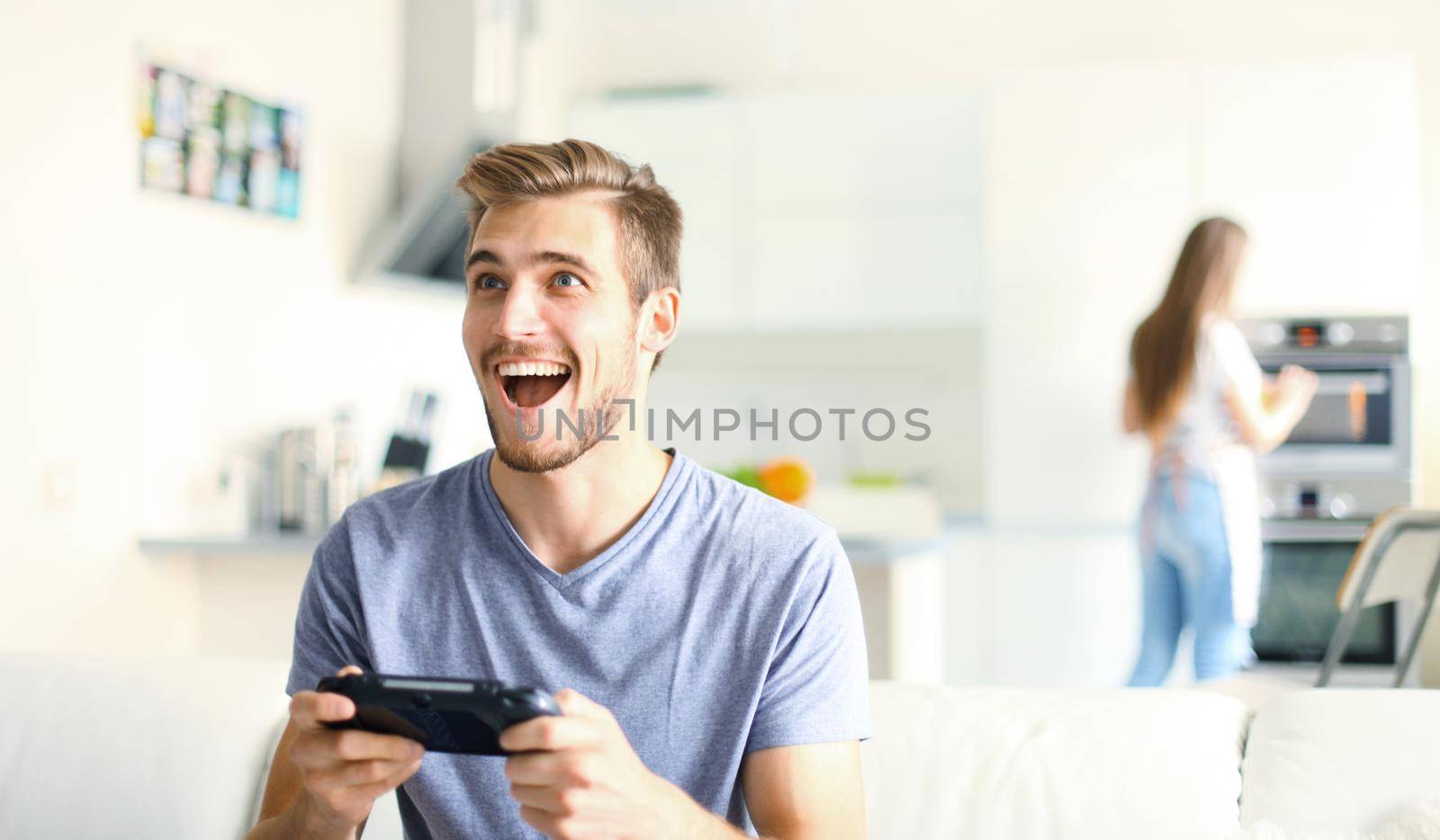 Man playing video games while his girlfriend cooking in the kitchen