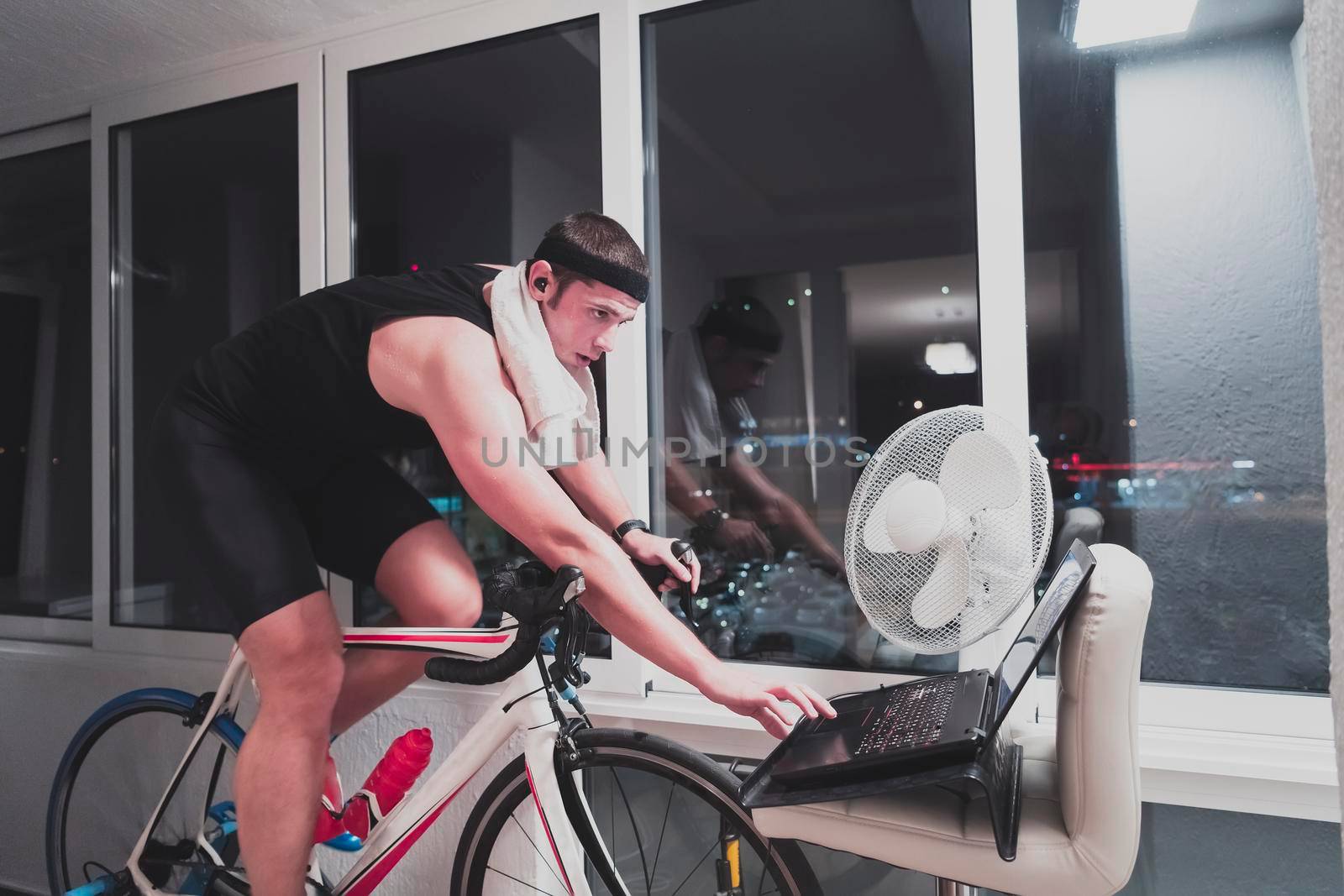 Man cycling on the machine trainer he is exercising in the home at night playing online bike racing game by dotshock