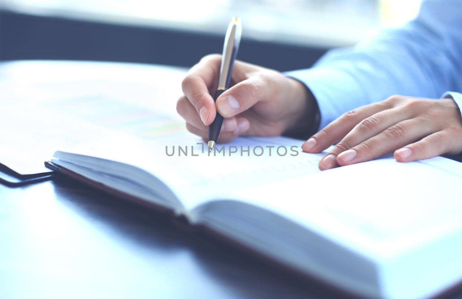 Female hand holding pen ready to make note in opened notebook sheet.