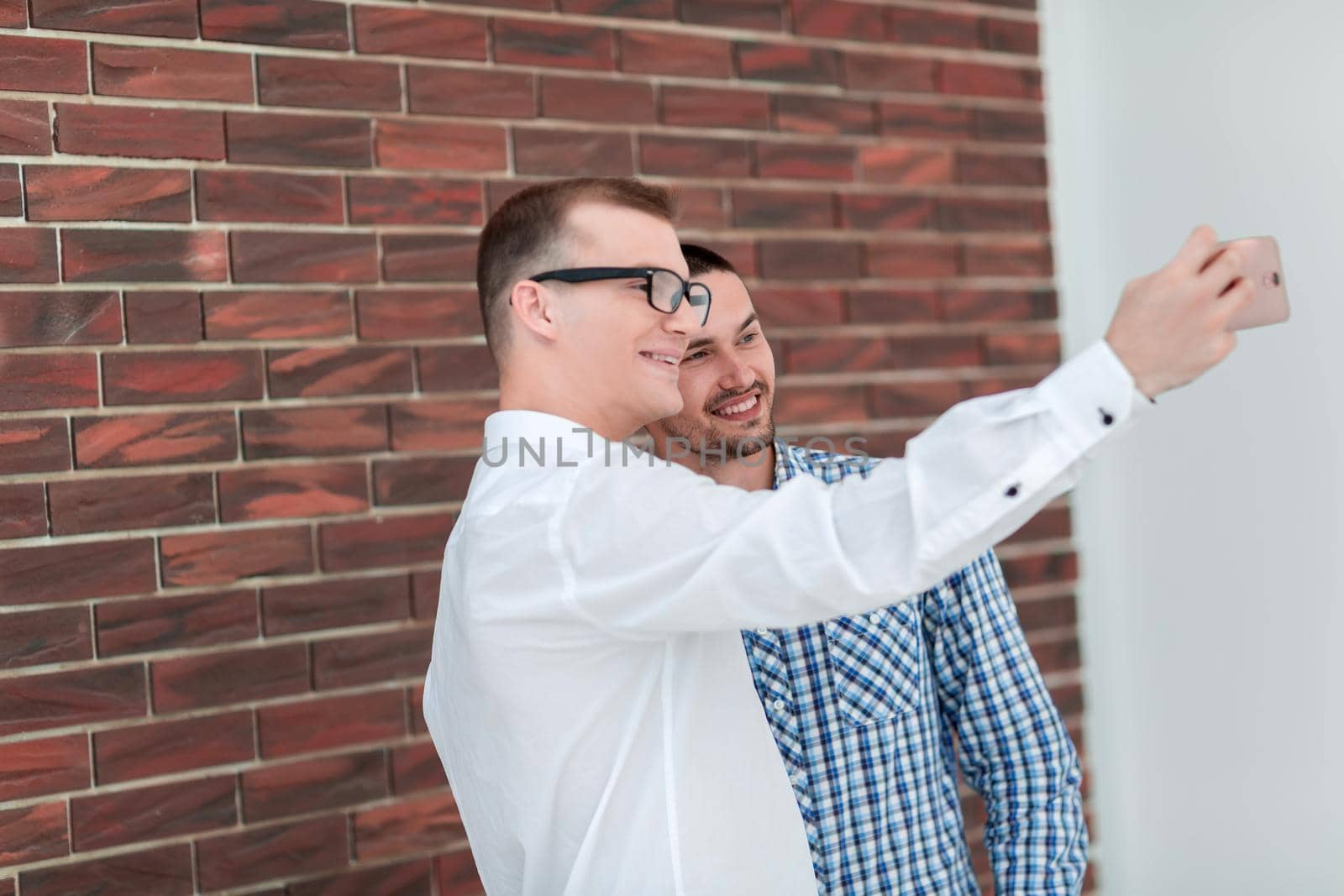 two young men taking selfies standing near a brick wall .people and technology